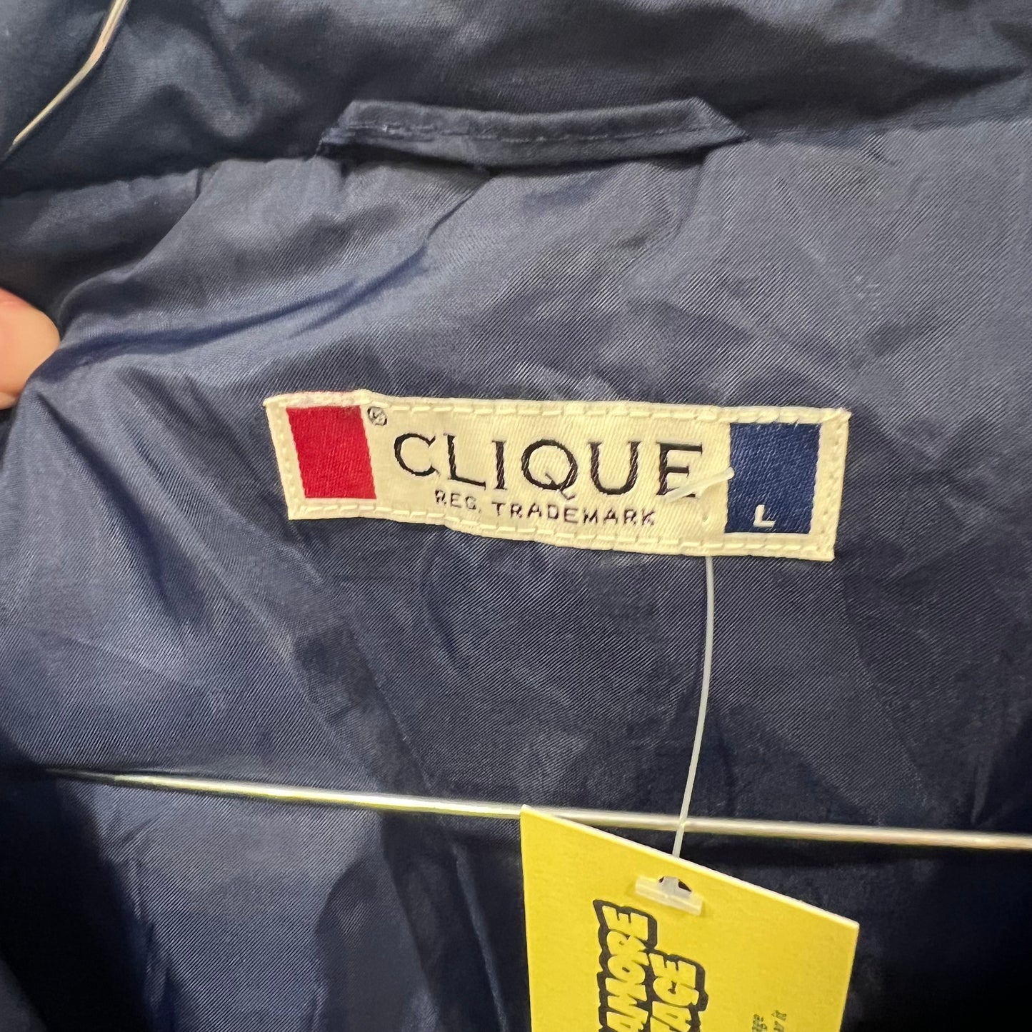 Navy blue jacket with 'Clique' label and yellow tag on a hanger