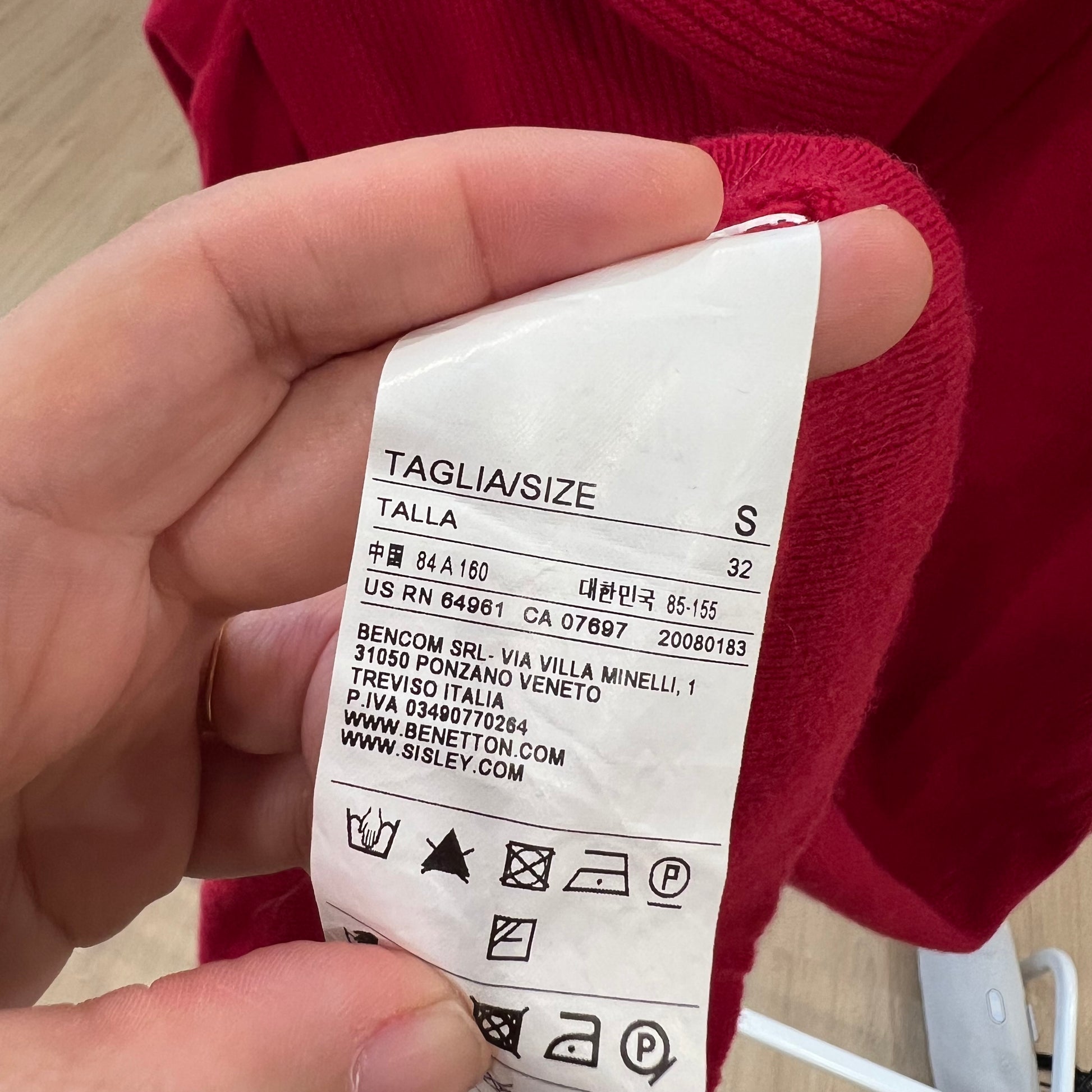 Hand holding a clothing tag with size information against a red garment background