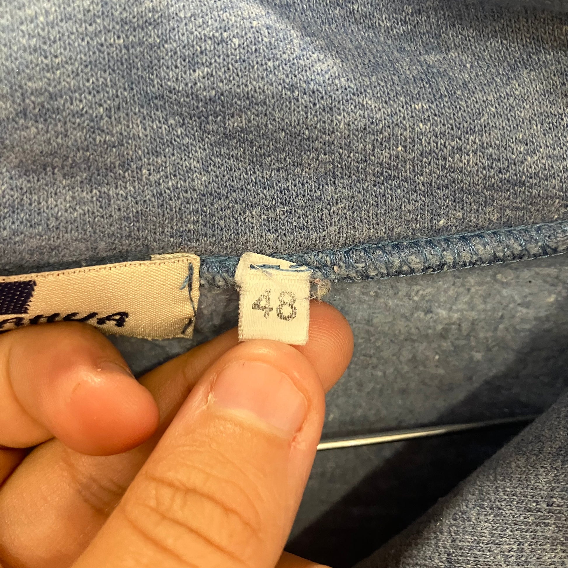 Close-up of a denim fabric with a size tag labeled '48' held by a hand