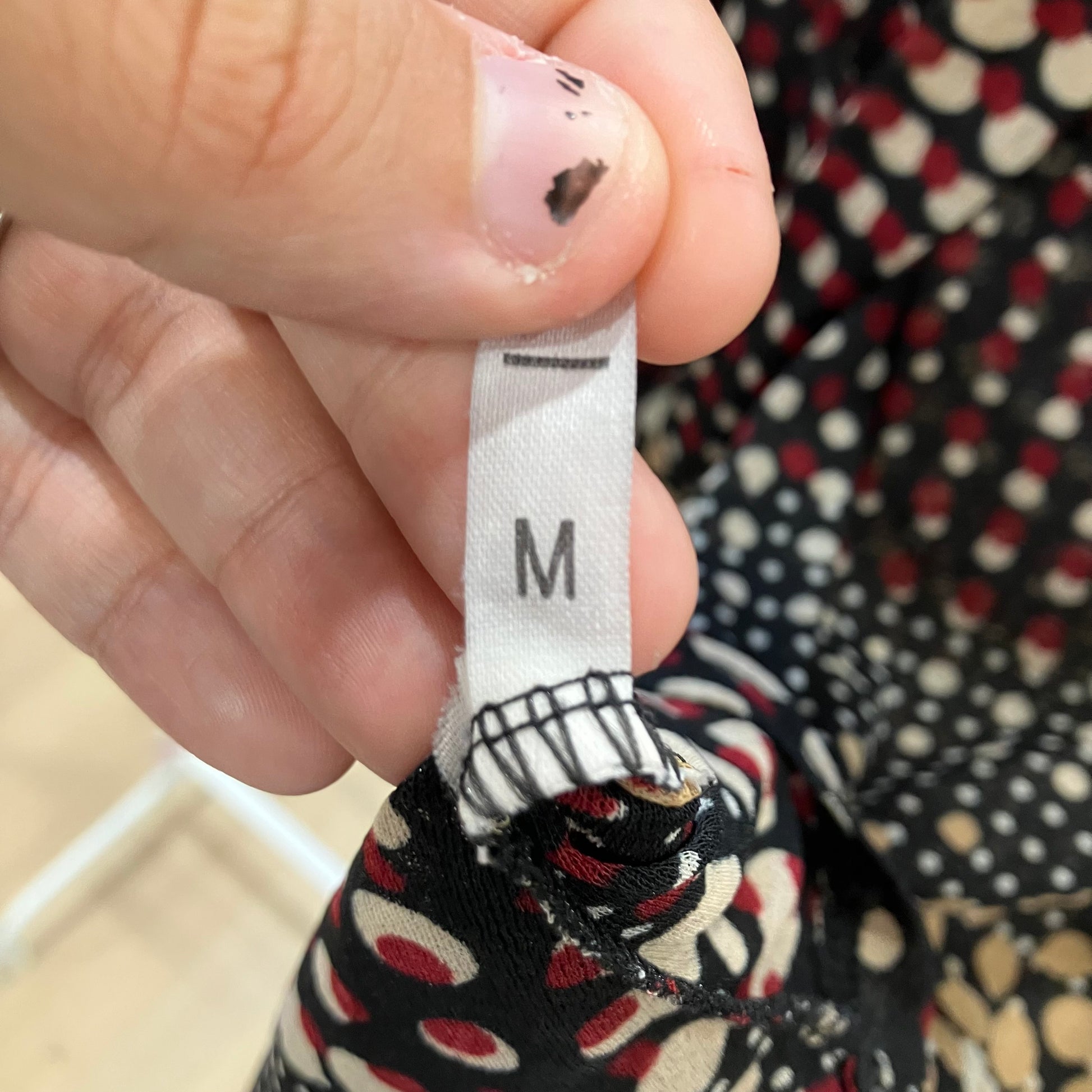Hand holding a patterned garment with a size label showing 'M'