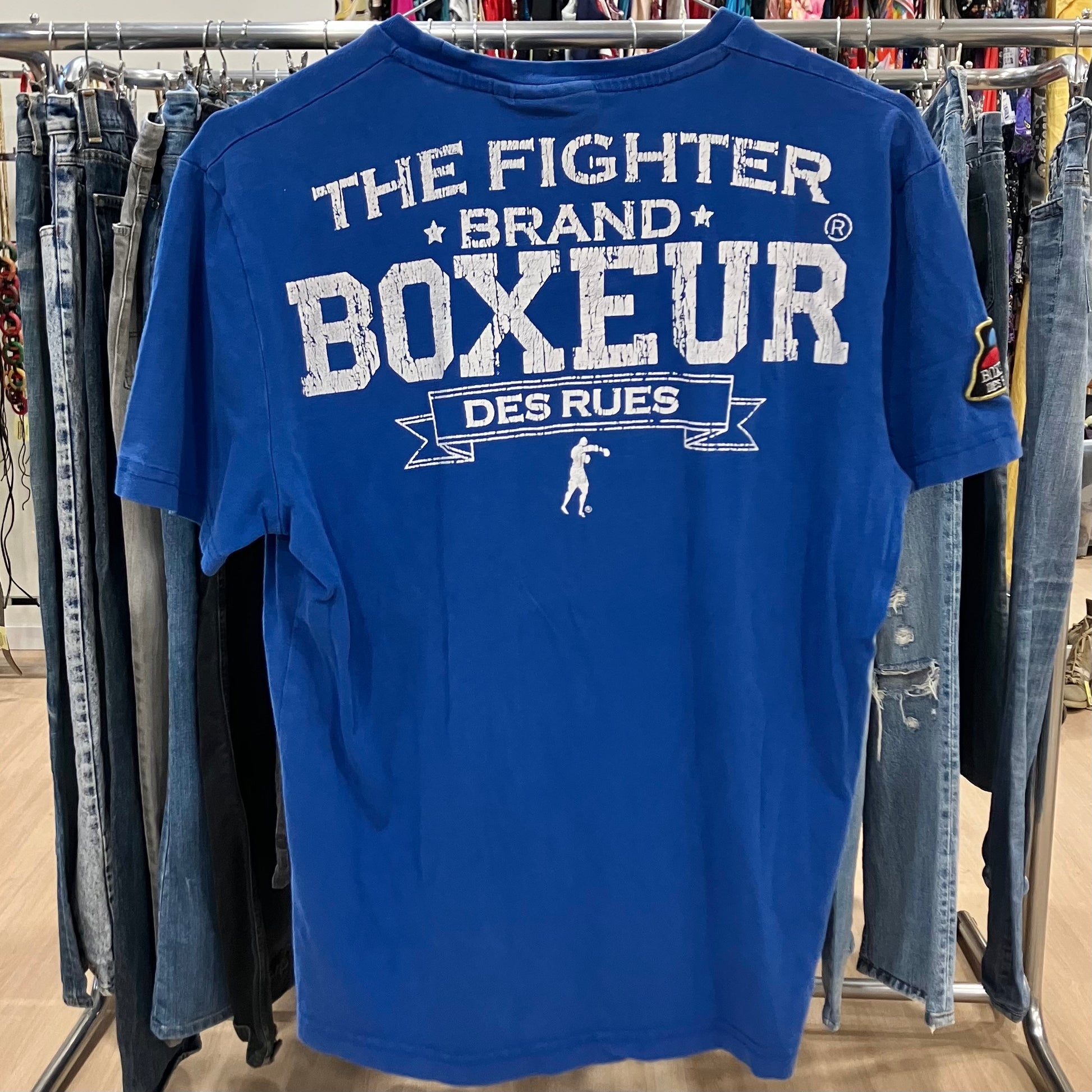 Blue t-shirt with 'The Fighter Brand Boxeur Des Rues' text on a clothing rack