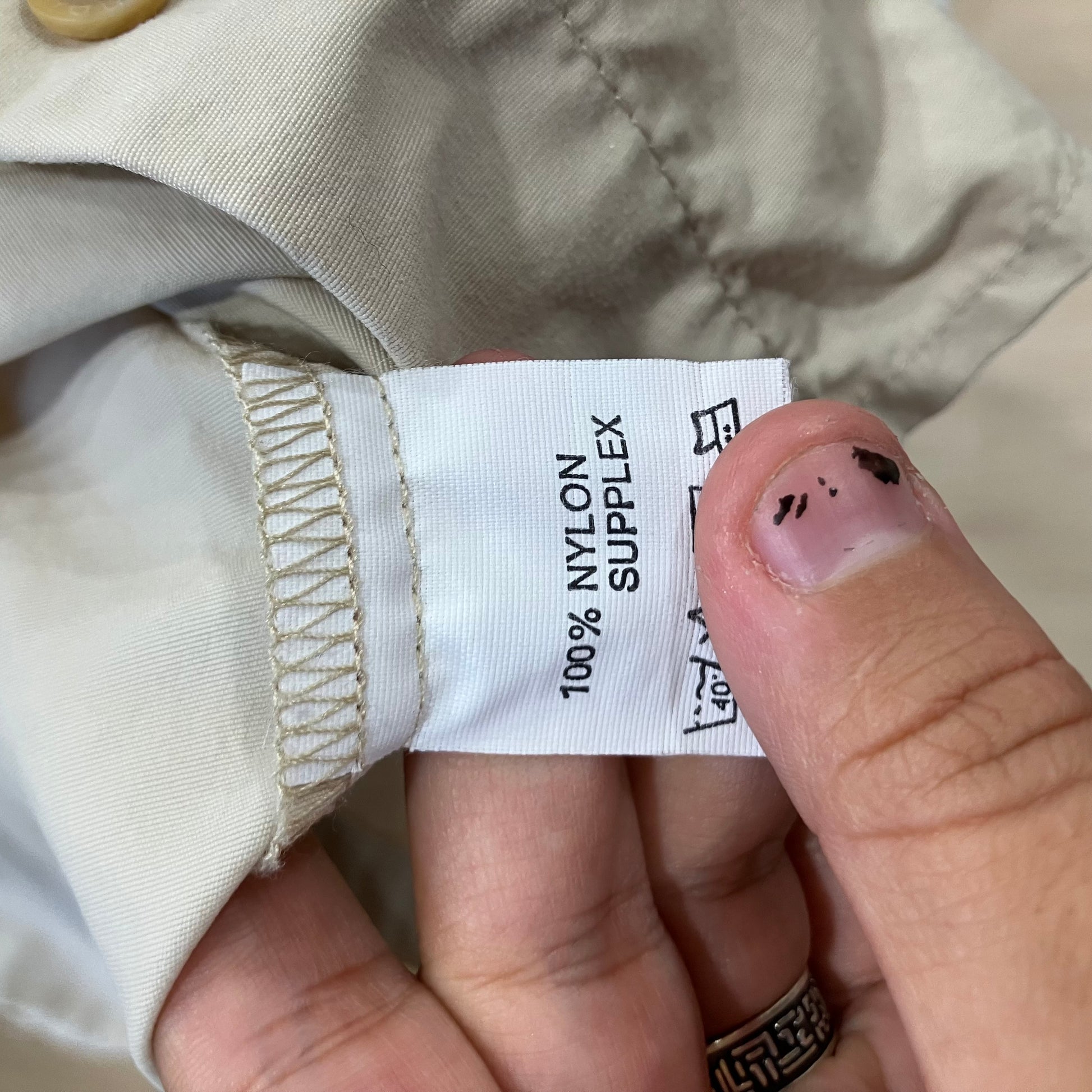 Hand holding a label on beige fabric with '100% Nylon Supplex' text