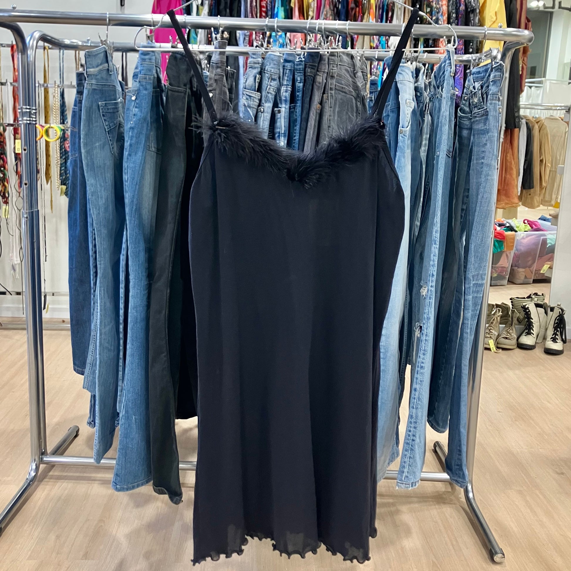 Black dress with  on a clothing rack with jeans in a store setting
