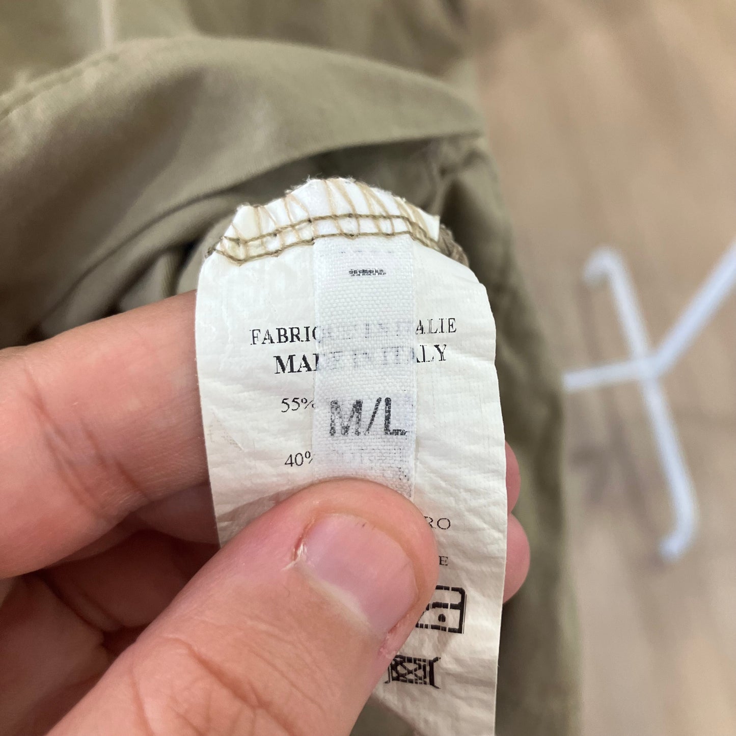 Fabric composition label held by a hand with a beige jacket in the background