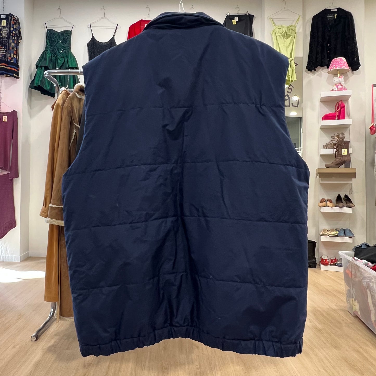 Navy puffer vest displayed in a store with clothing racks and shelves in the background