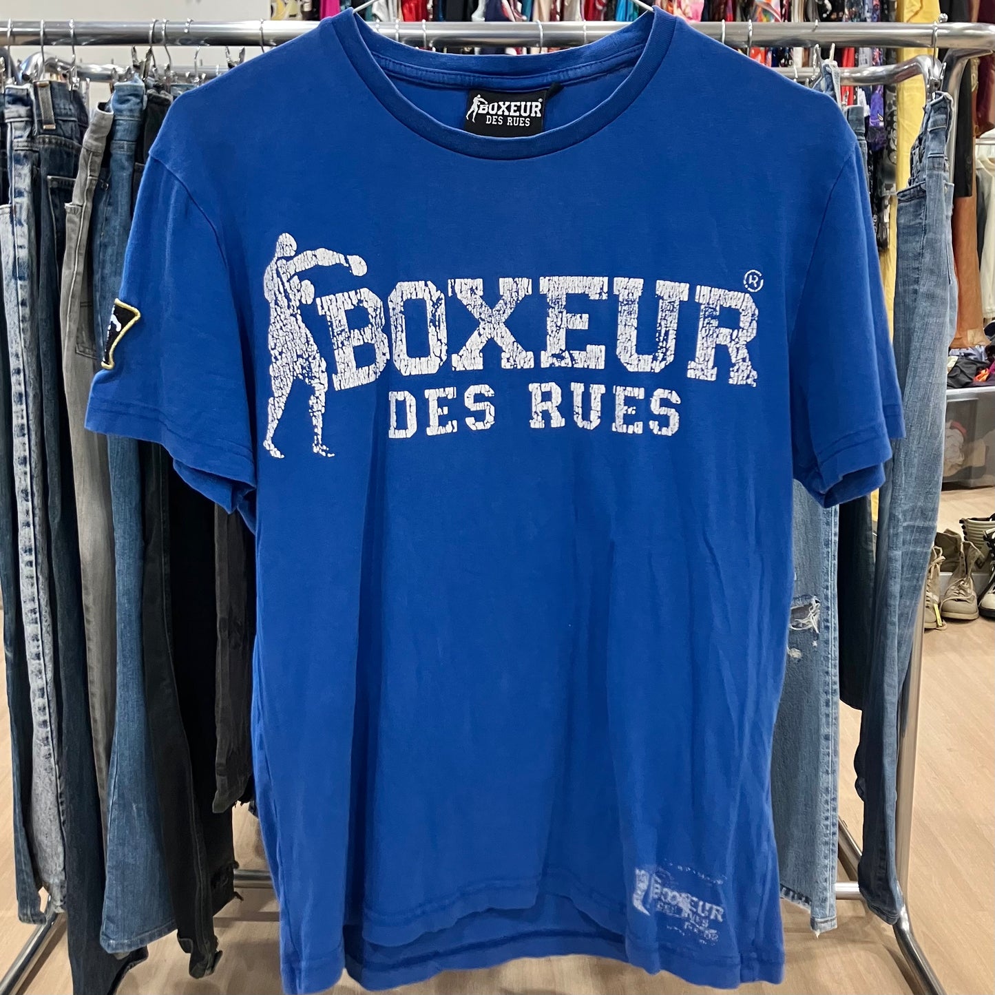 Blue t-shirt with 'Boxeur des Rues' text and logo on a clothing rack