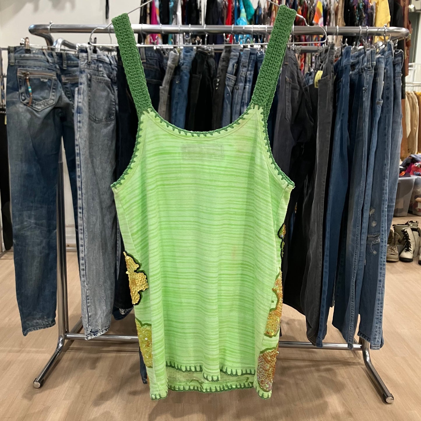 Green tank top with green straps hanging on a rack with jeans
