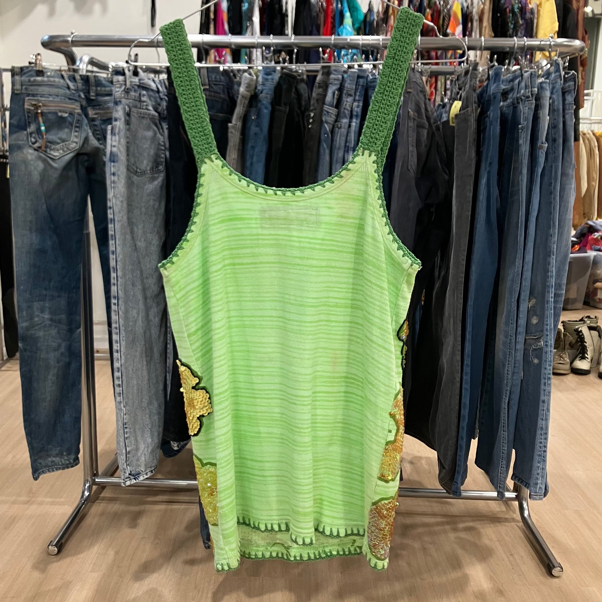 Green tank top with green straps hanging on a rack with jeans