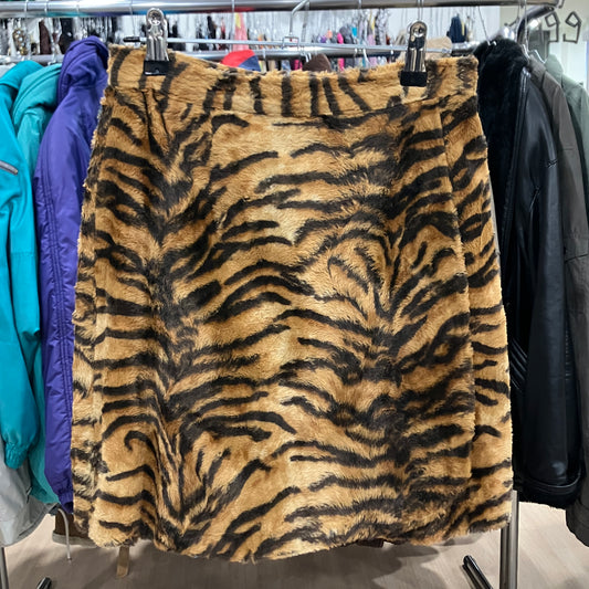 Faux fur mini skirt with a bold tiger print pattern in shades of brown and black, hanging on a clothing rack in a store