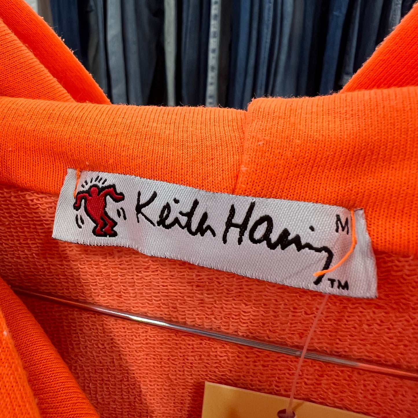 Close-up of an orange garment with a Keith Haring label