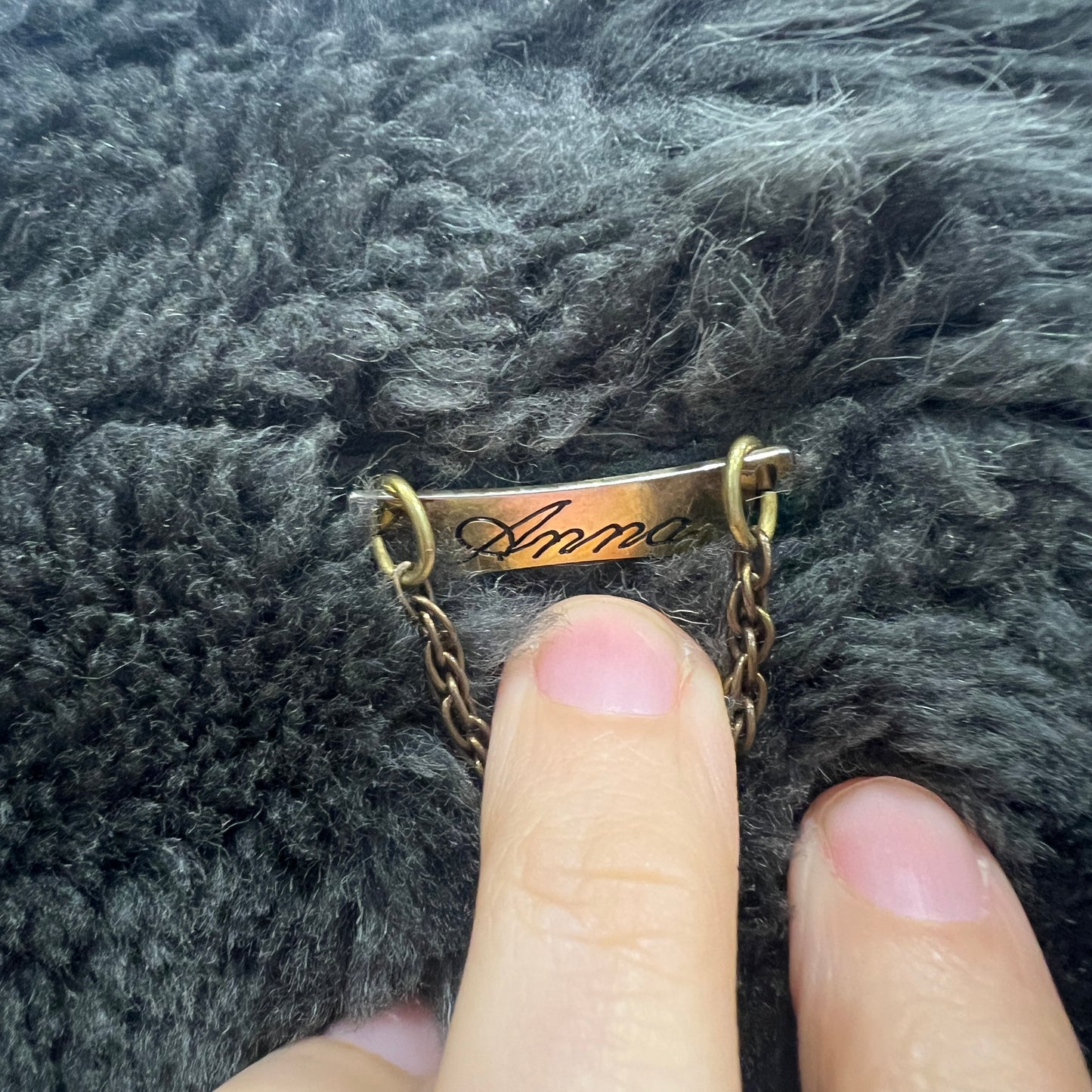 Gold name tag with 'Anna' engraved on a textured gray fabric background