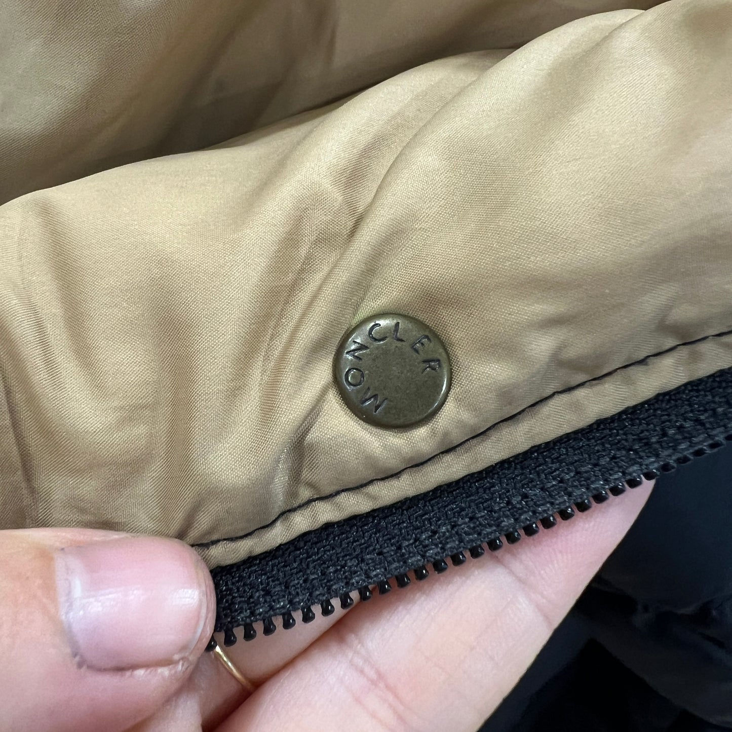 Close-up of a jacket with a zipper and a brand logo, held by a hand
