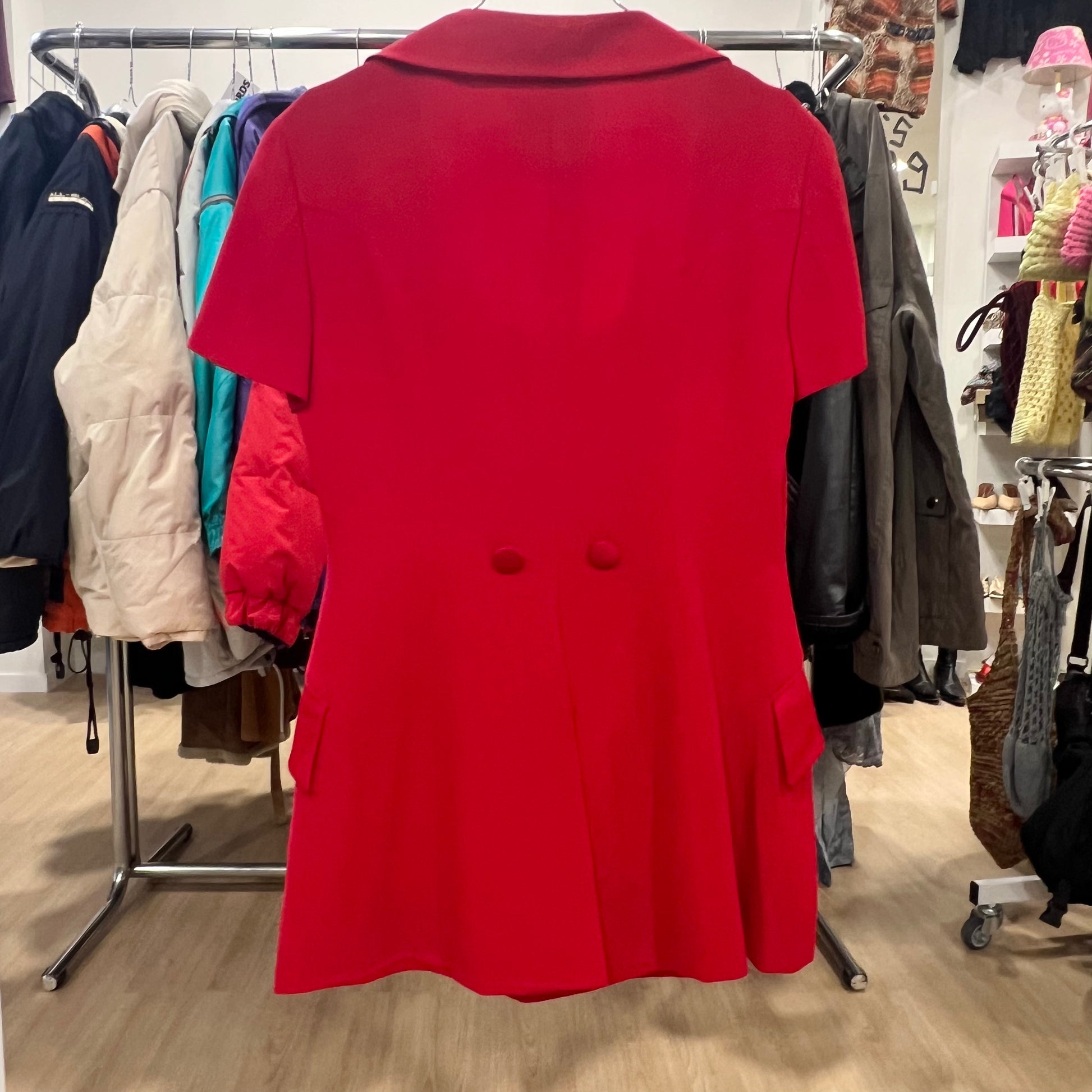 Red coat displayed in a clothing store with racks of other coats in the background