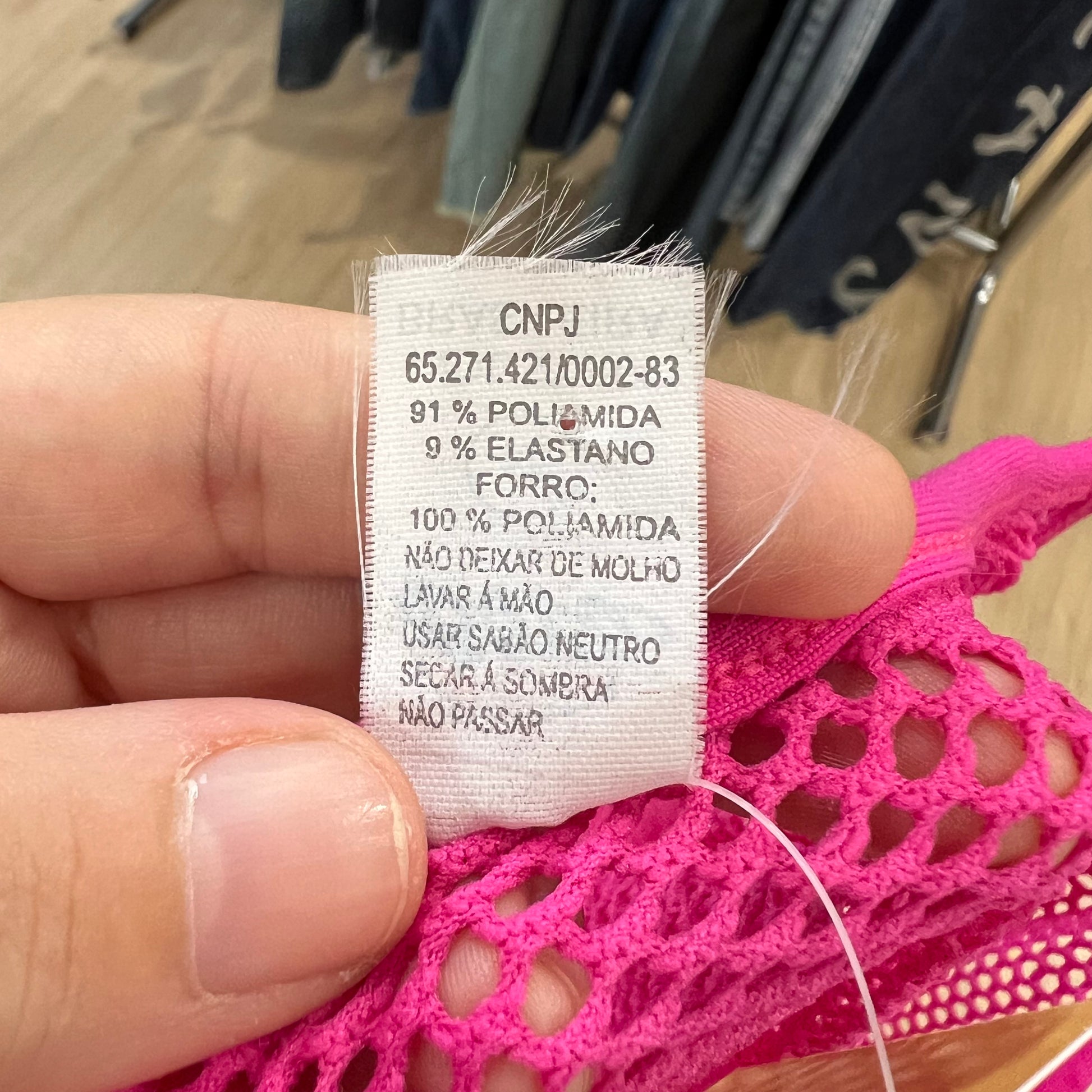 Clothing label held by a hand with pink lace fabric in the background