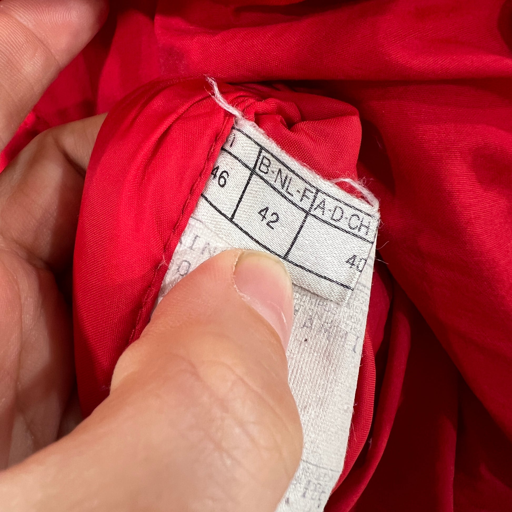 Close-up of a red garment with a size label held by a hand