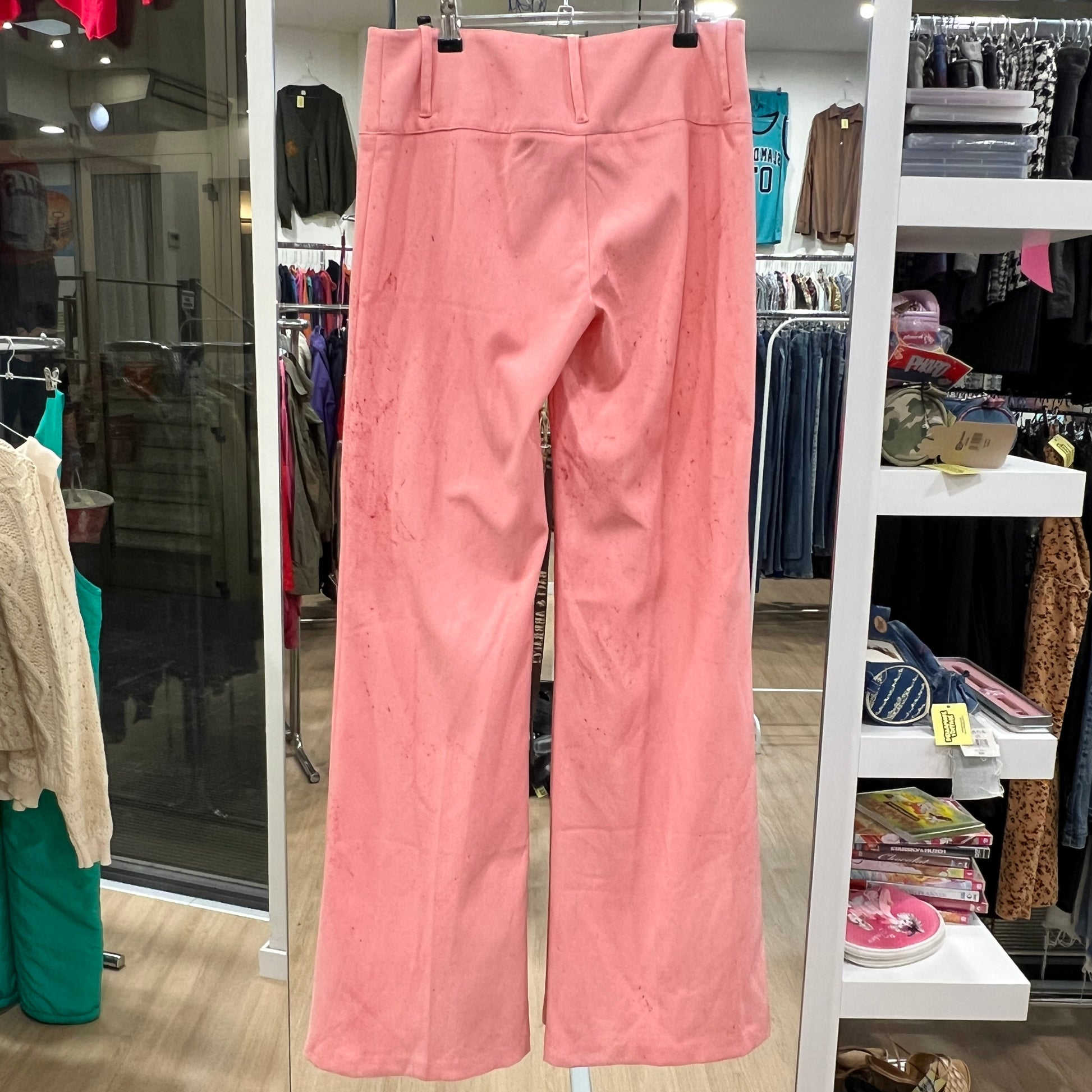 Pink pants hanging on a rack in a store setting with various clothing items in the background