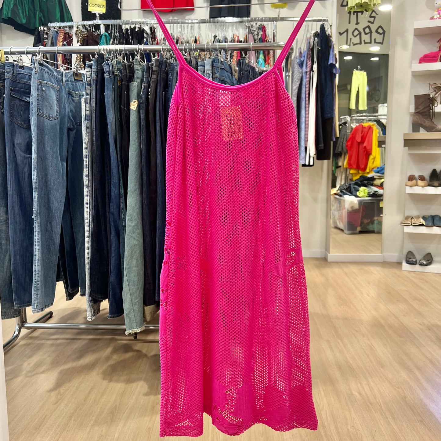 Pink lace dress hanging on a rack in a store with jeans and other clothing in the background