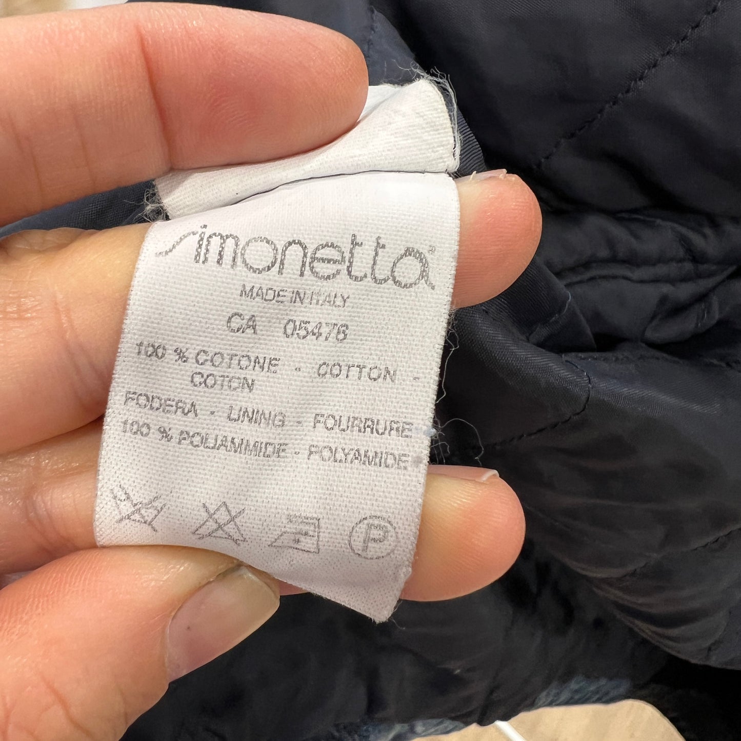 Close-up of a clothing label held by a hand, with a dark fabric background 