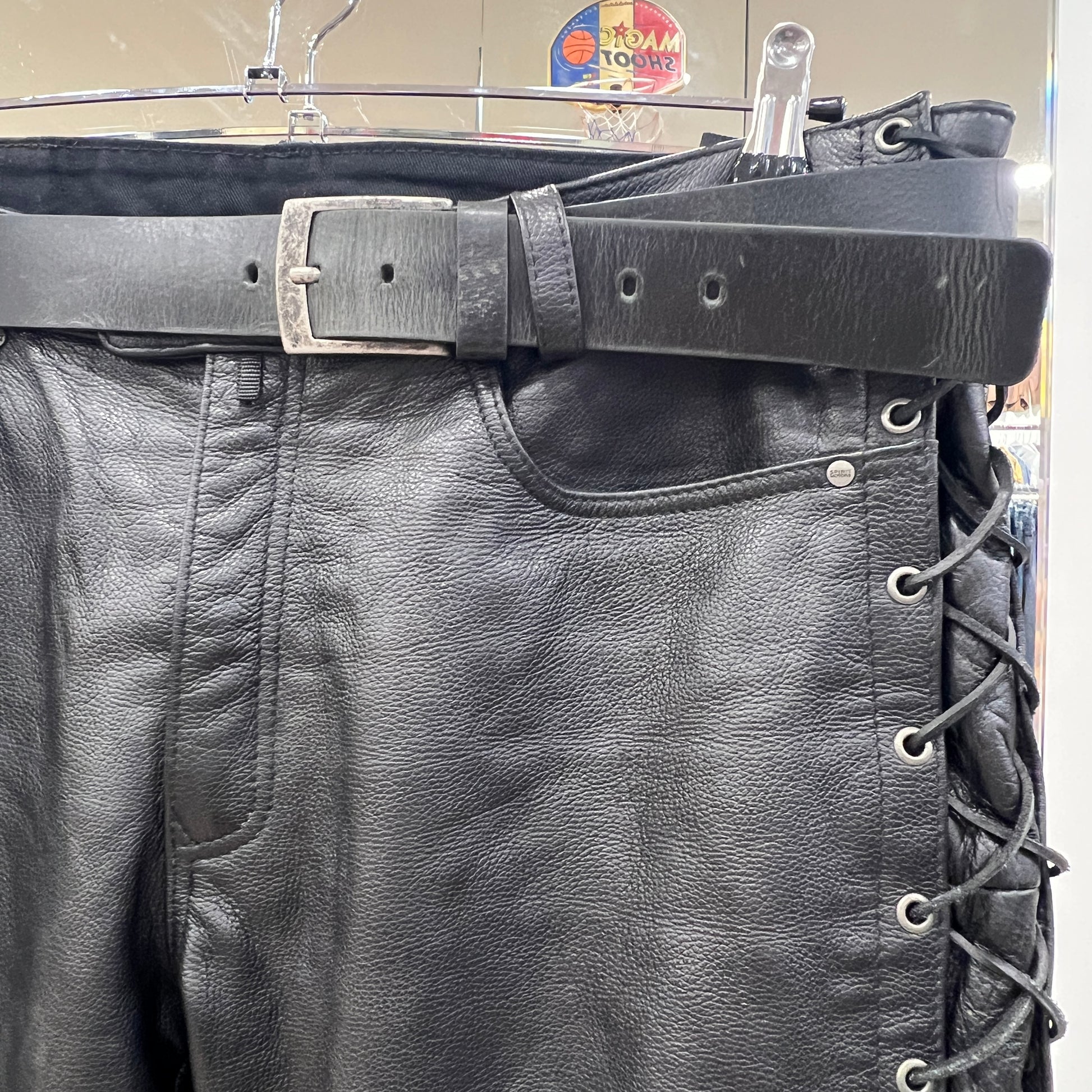 Close-up of black leather pants with a belt and lace-up design, hanging on a rack