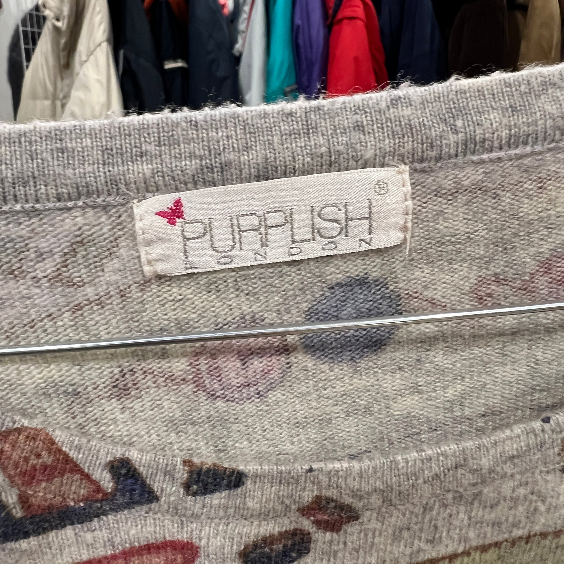Textile product with 'PURPLISH LONDON' label against a background of clothes on hangers
