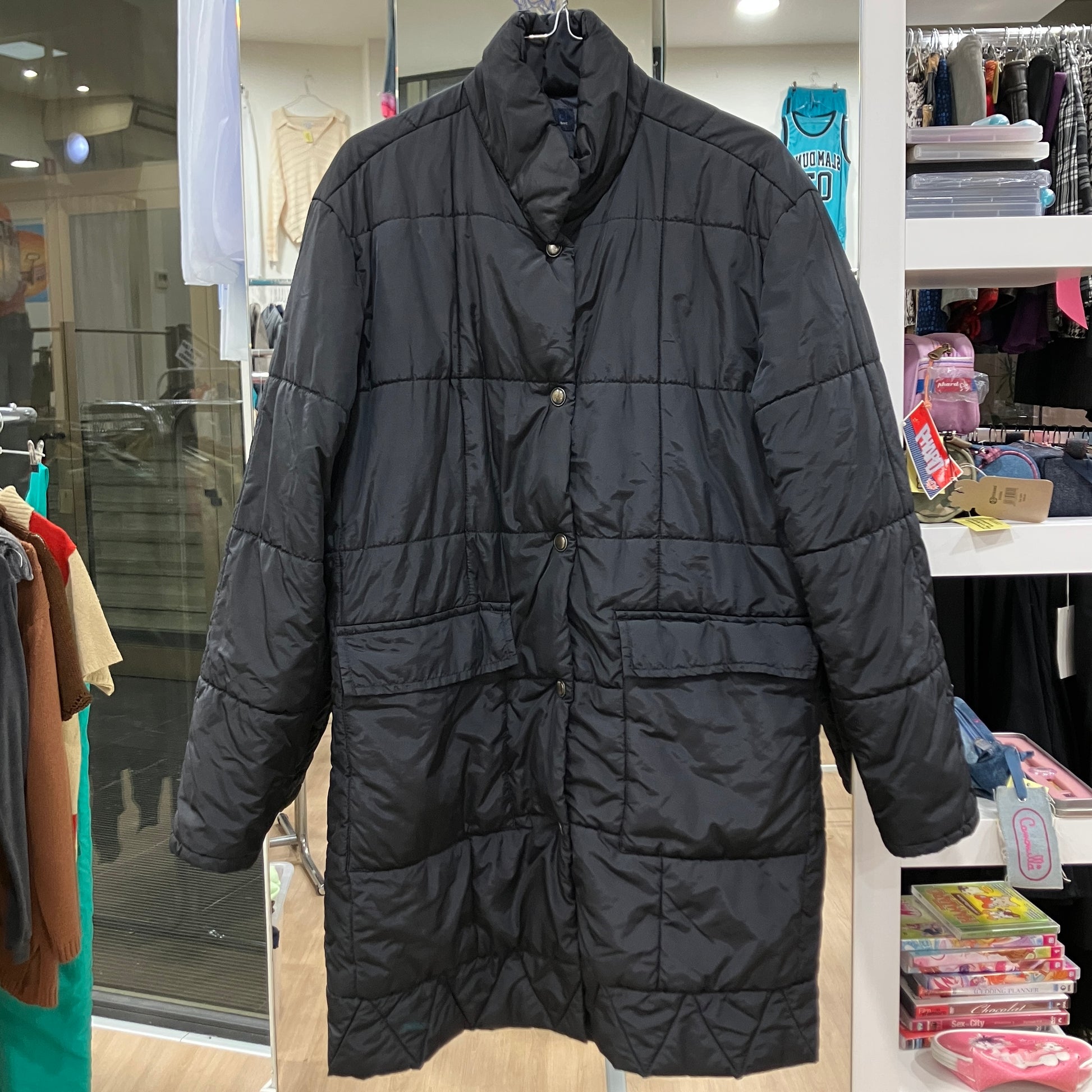Black puffer coat hanging in a store with clothing racks and shelves in the background