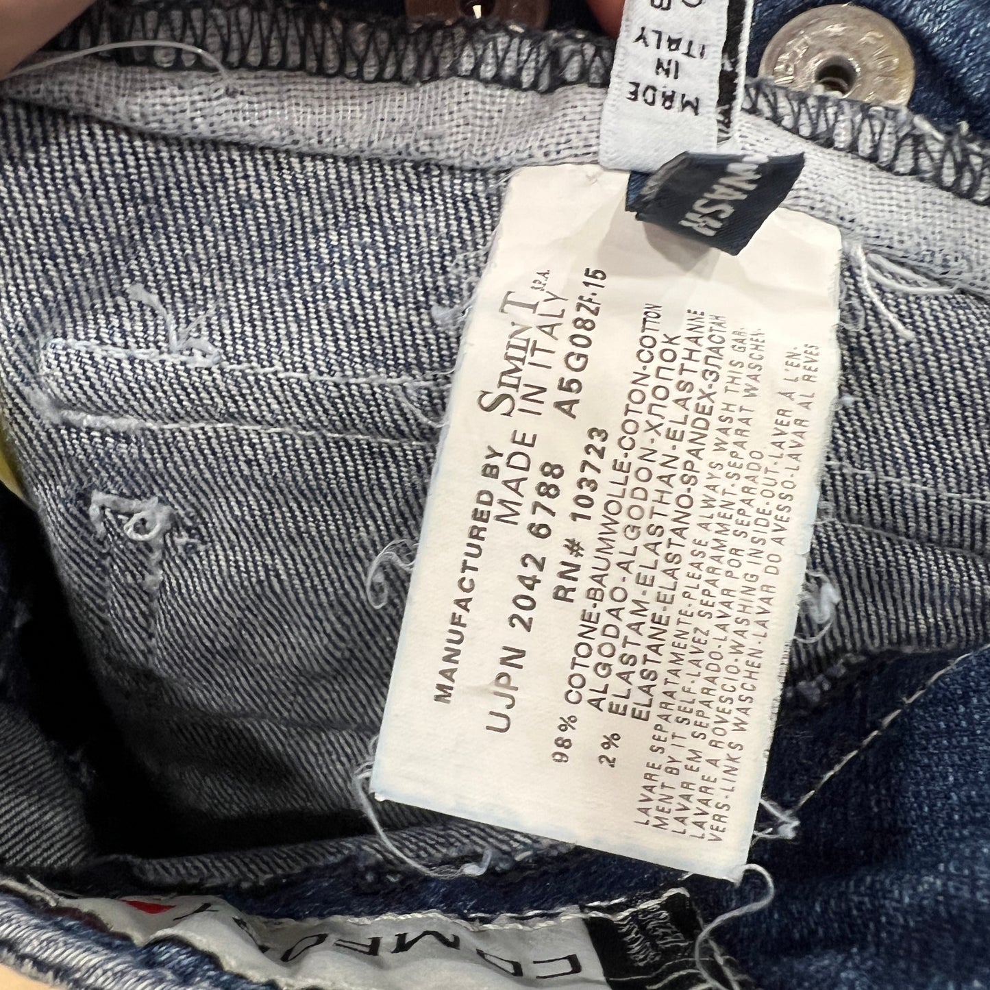 Close-up of an Armani Jeans interior care label showing the fabric composition and manufacturing details, with frayed denim visible around the tag
