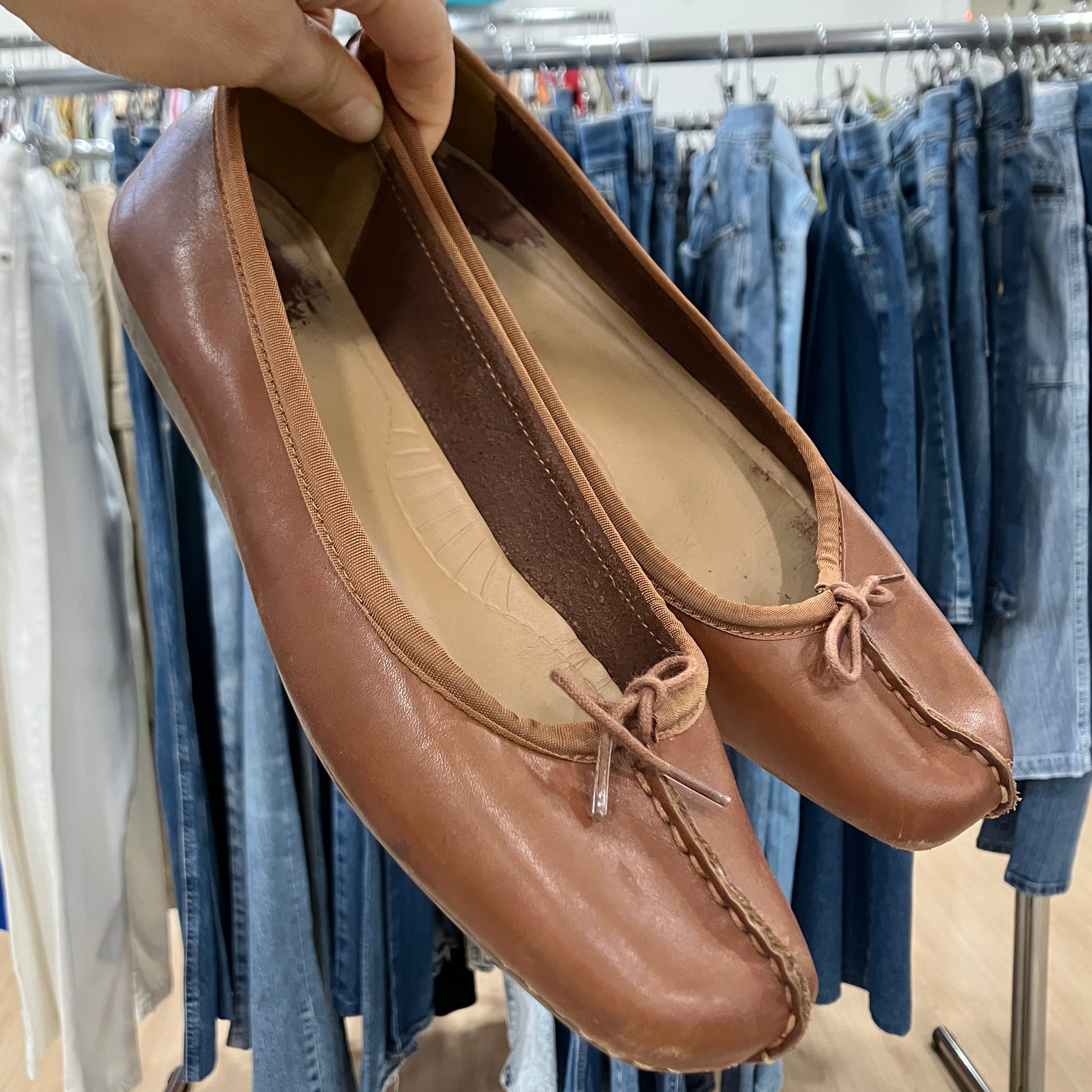 Brown leather shoes held in front of a clothing rack with jeans