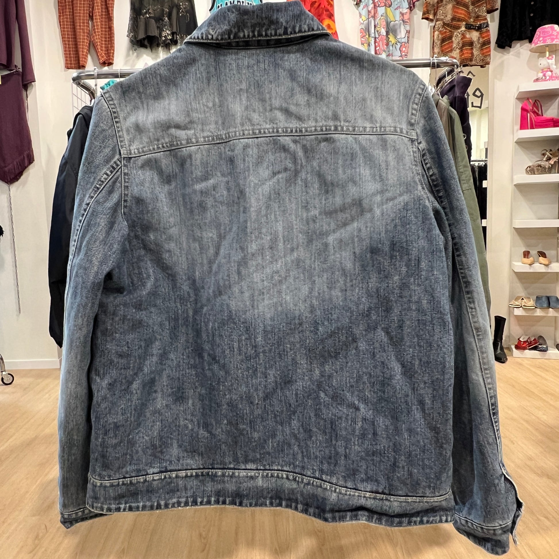 Blue denim jacket in a store setting with clothing racks and shelves in the background