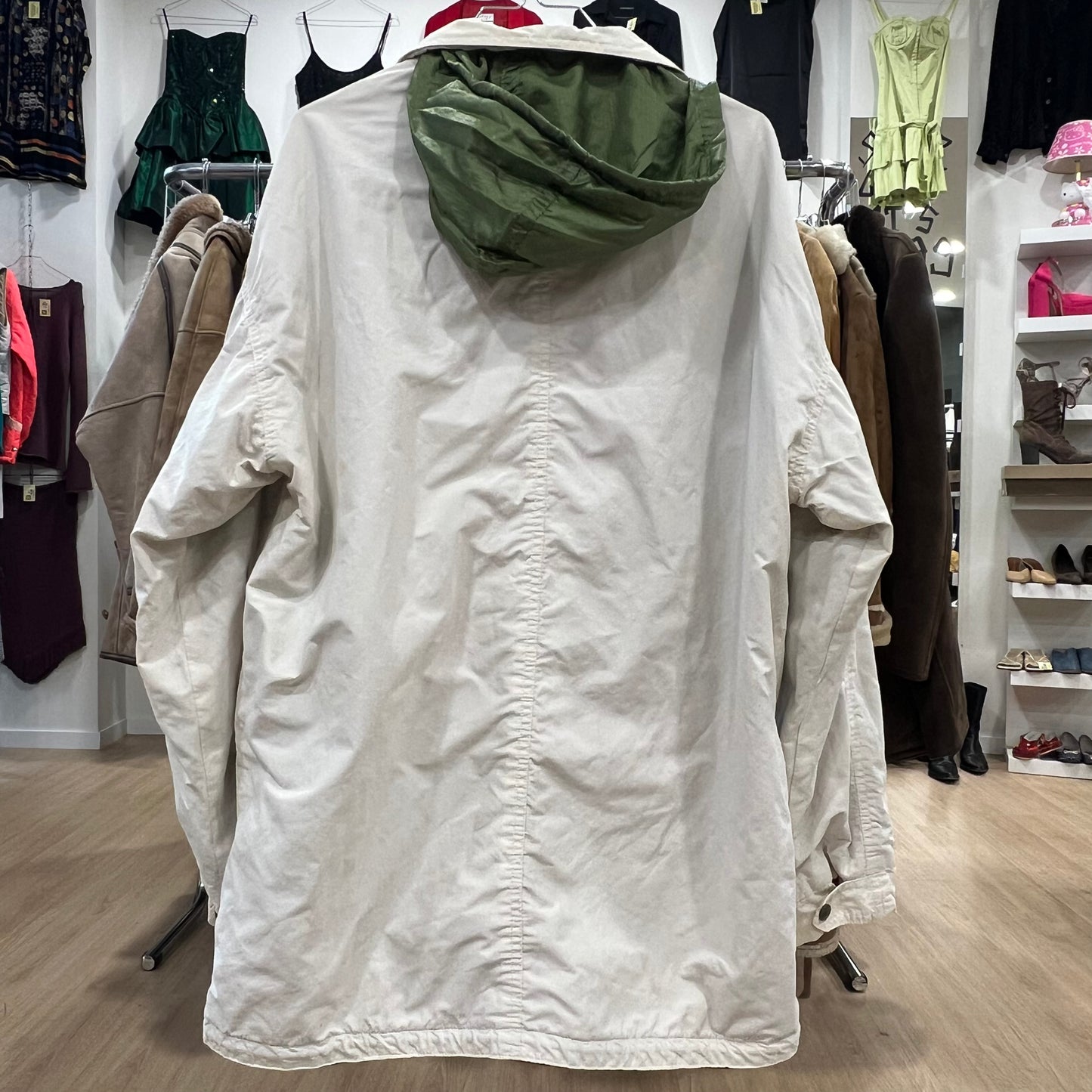 White jacket with green hood on a hanger in a store setting