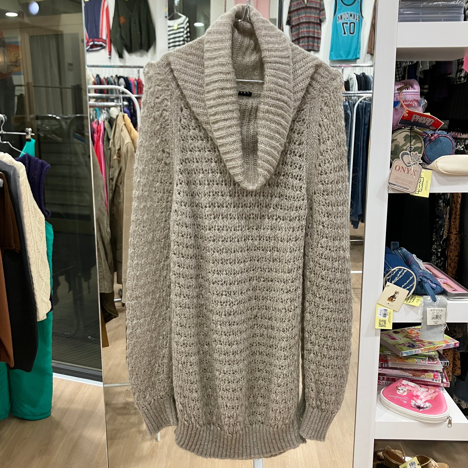 Gray knitted cardigan hanging in a store with clothing racks and shelves in the background