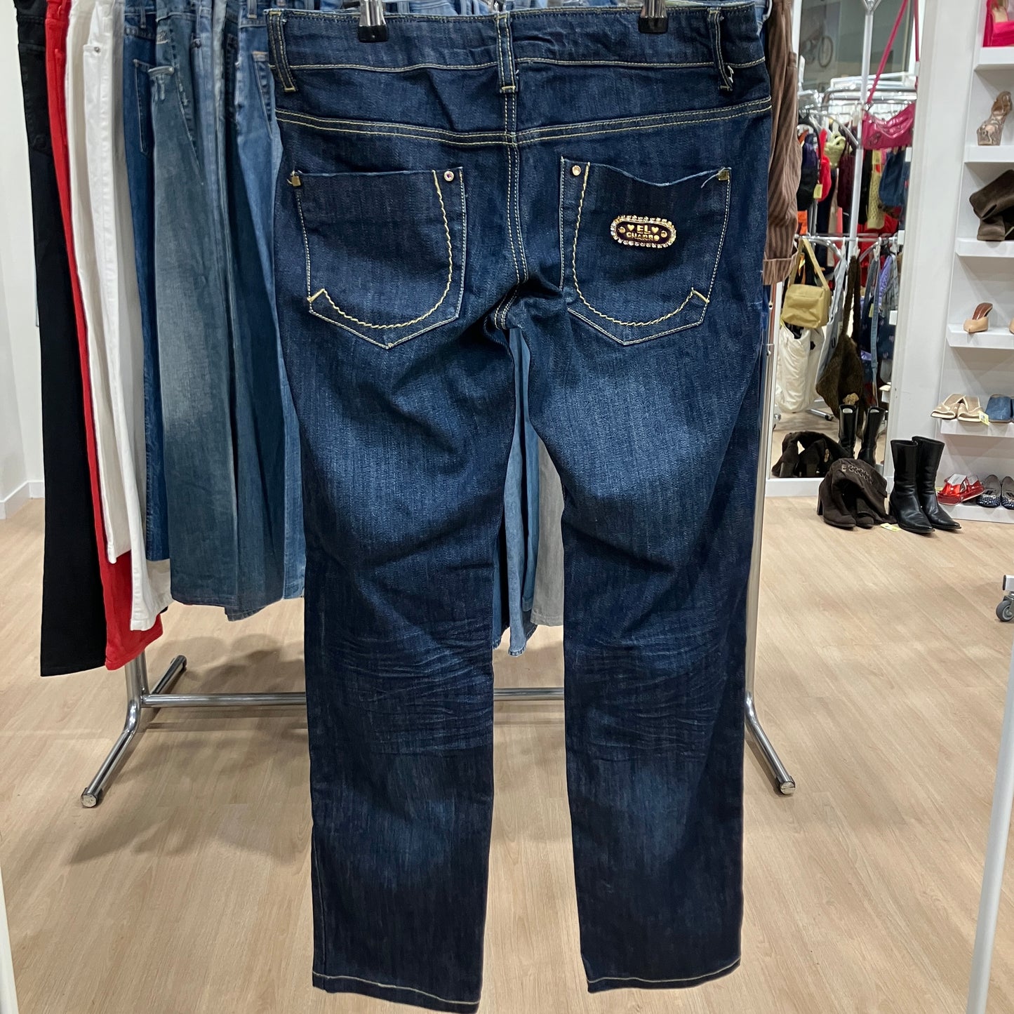 Blue jeans hanging on a rack in a store setting with various clothing and shoes in the background