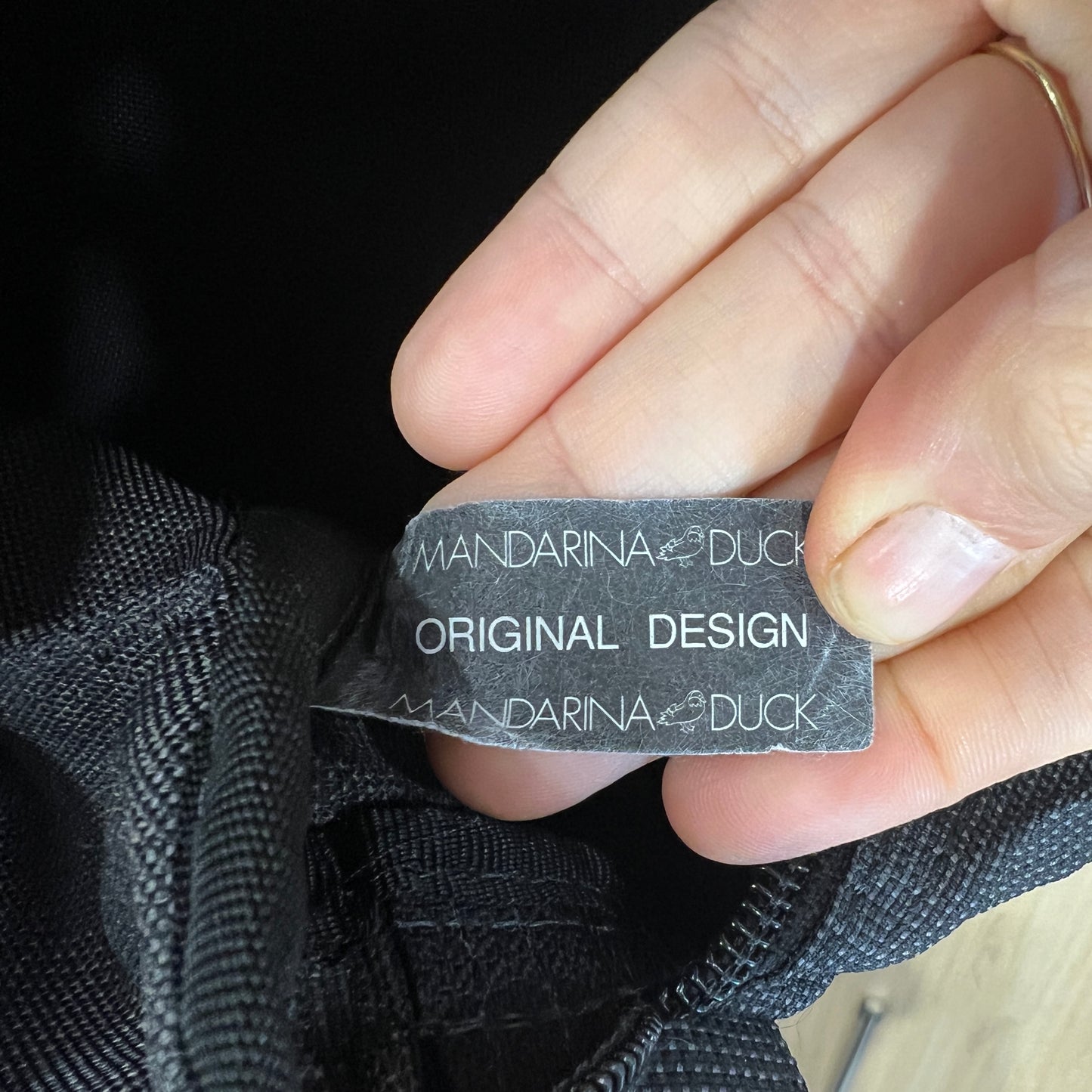 Hand holding a black label with 'Mandarina Duck' branding