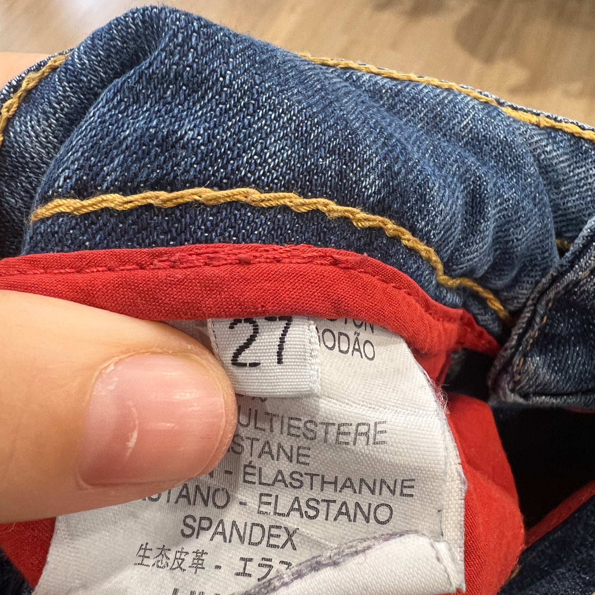 Close-up of a jeans label with a hand holding it, showing fabric details