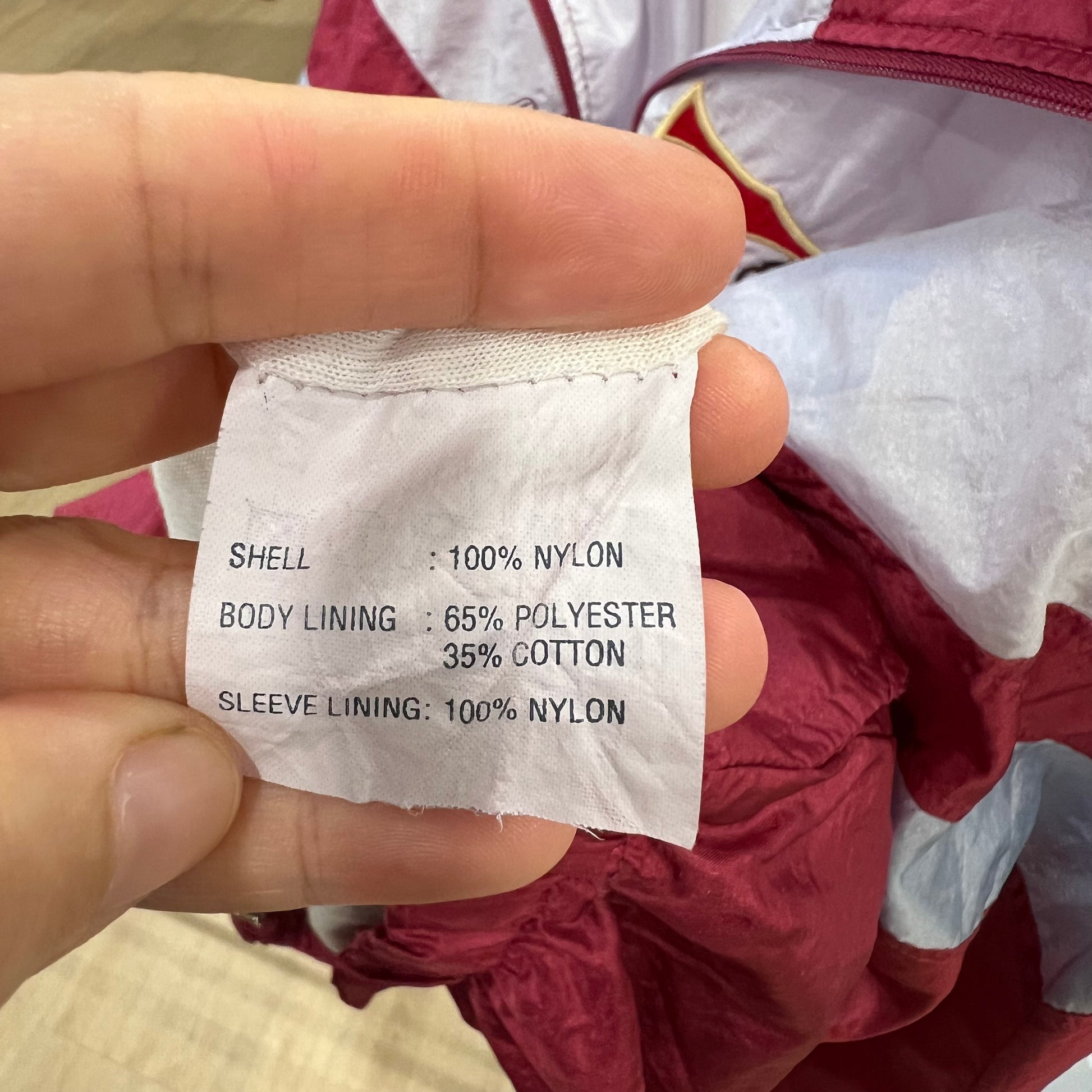 Hand holding a fabric composition label on a red jacket with white lining