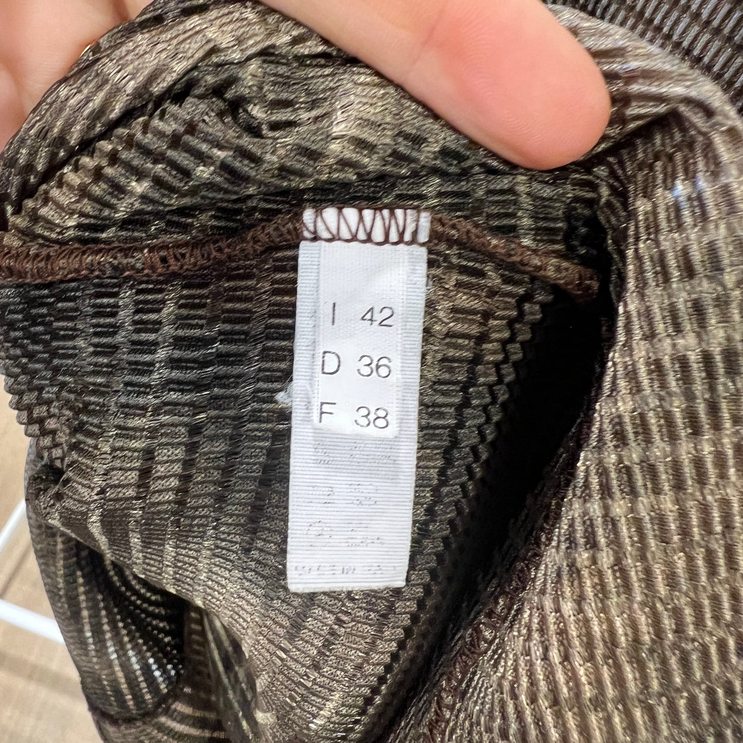 Close-up of a size tag inside a ribbed brown top, showing I 42, D 36, and F 38 while the fabric is held open with two fingers
