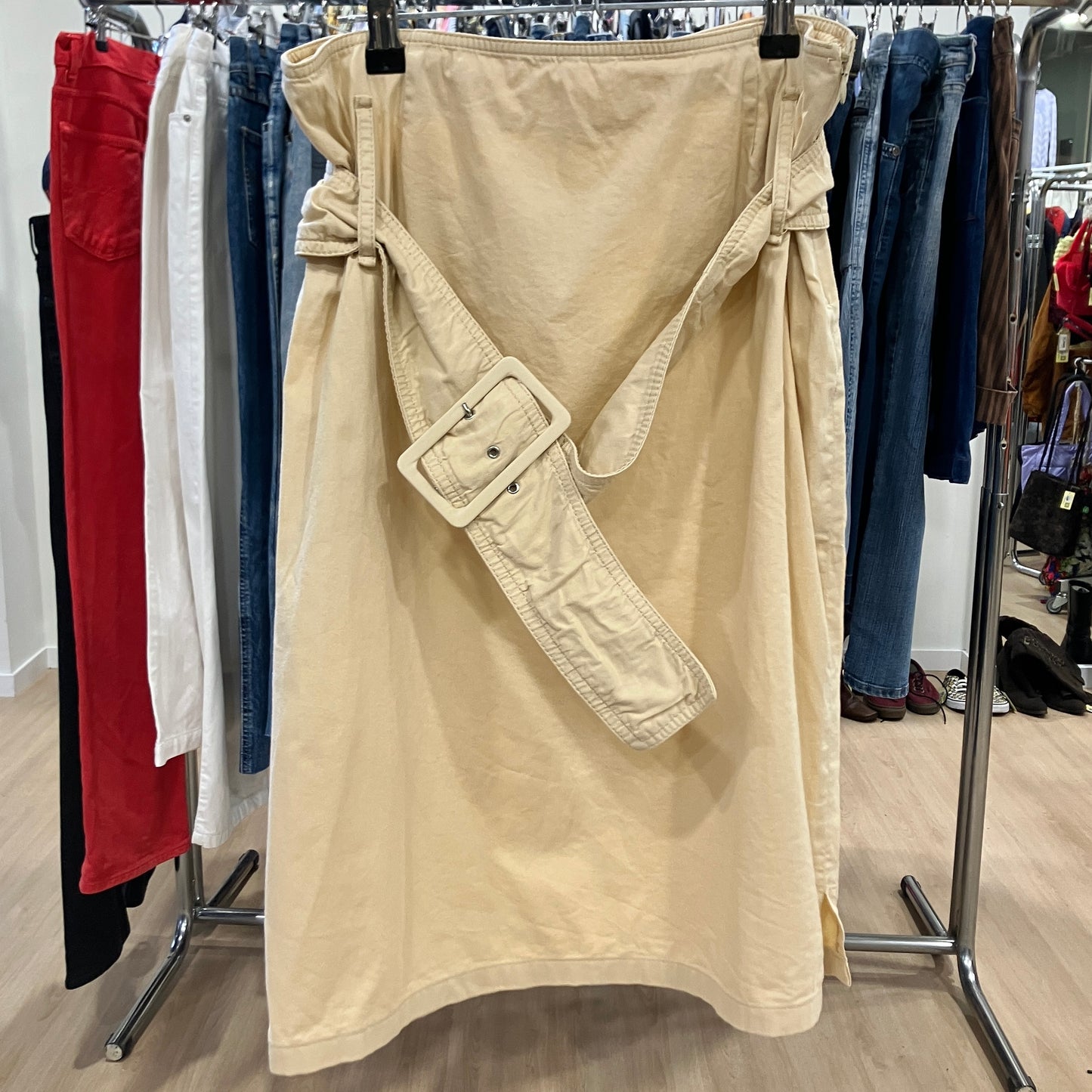 Beige wrap skirt with a large matching belt hanging on a rack inside a clothing store