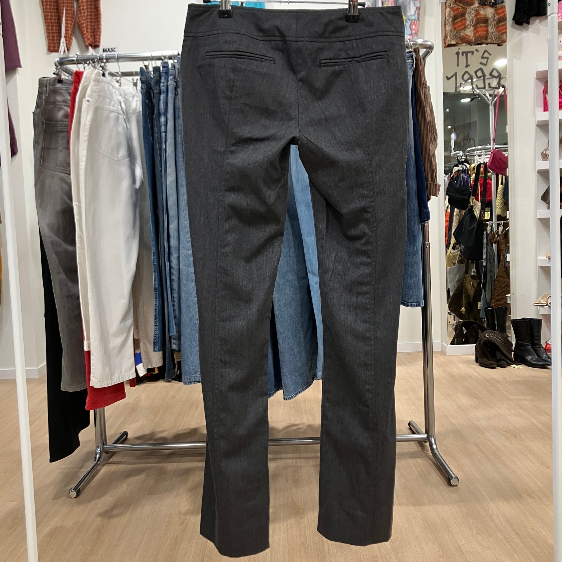 Black pants displayed on a rack in a store setting with various clothing items in the background