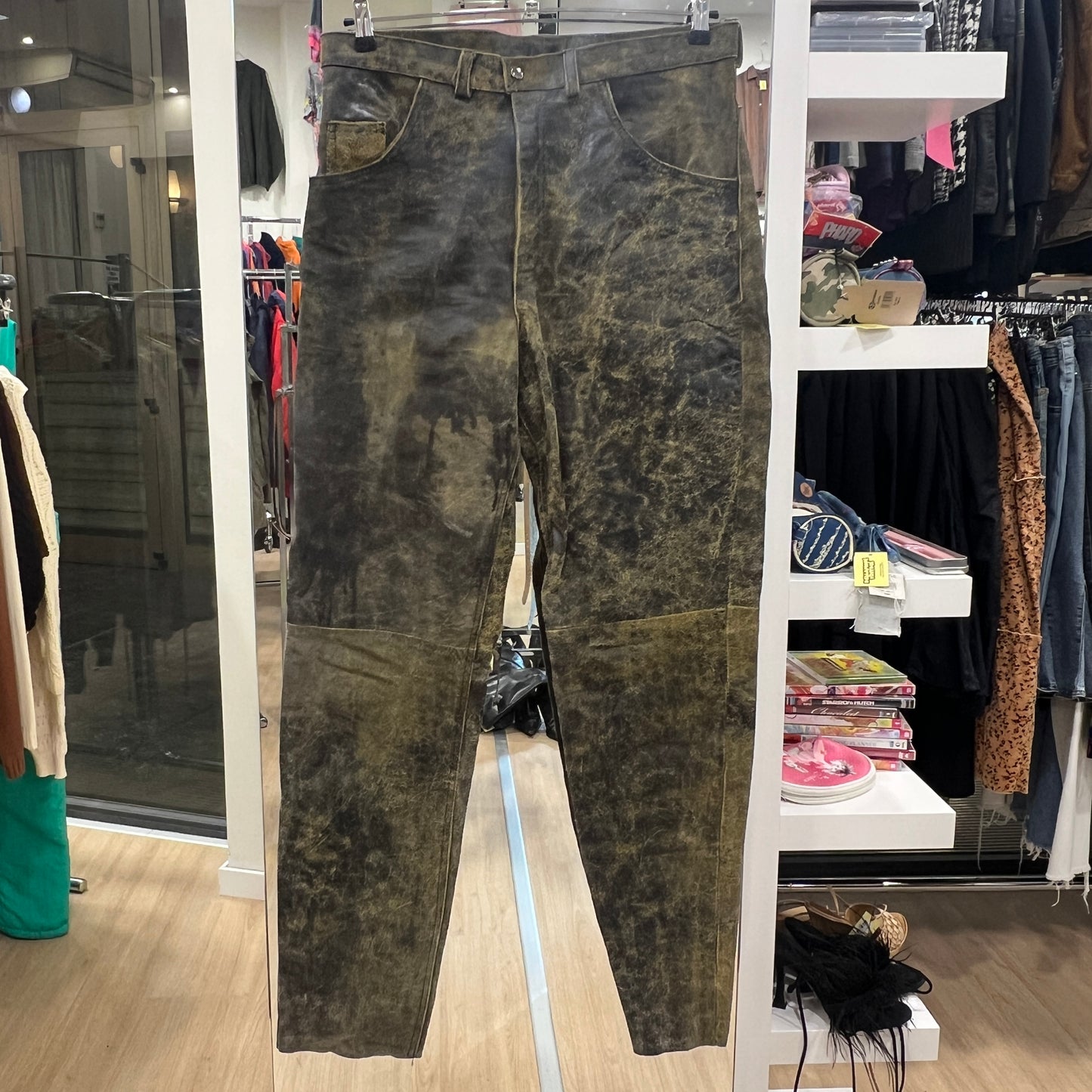 Distressed green-brown jeans hanging on a rack inside a clothing store