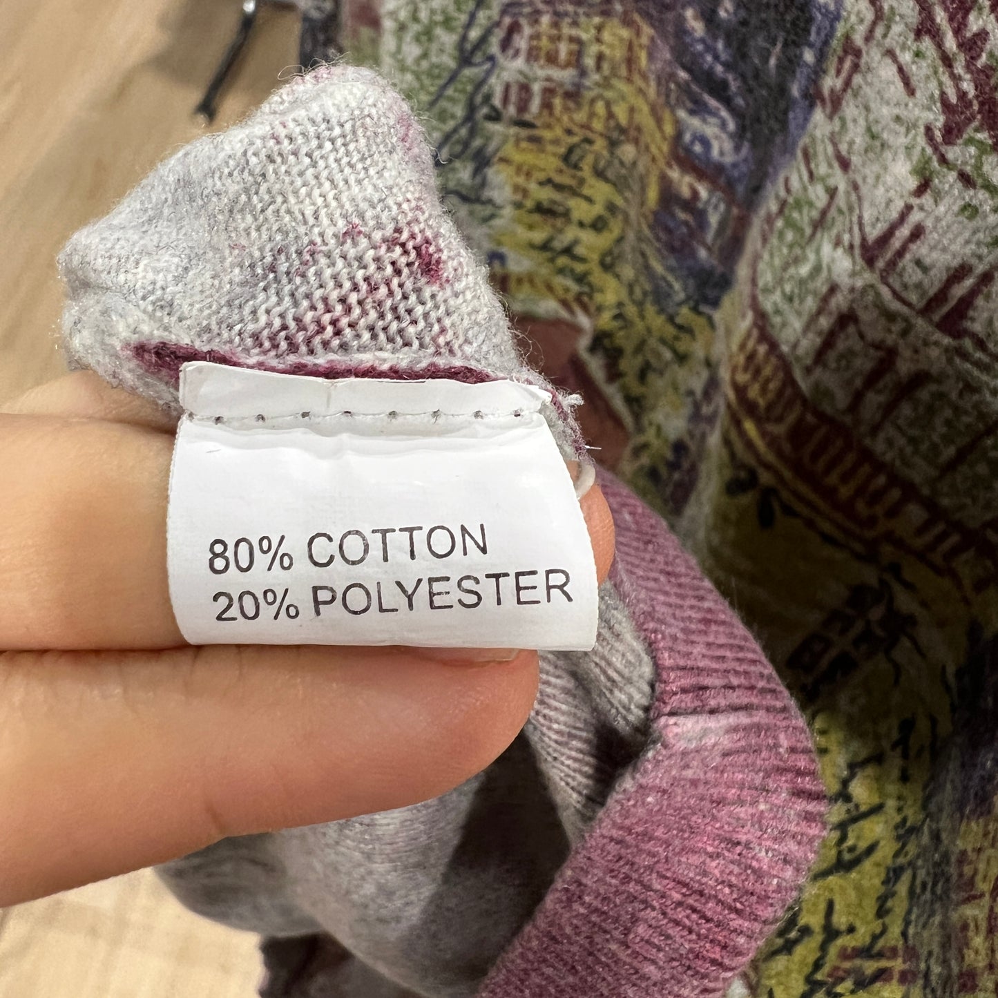 Hand holding a label with '80% Cotton, 20% Polyester' text against a textured fabric background