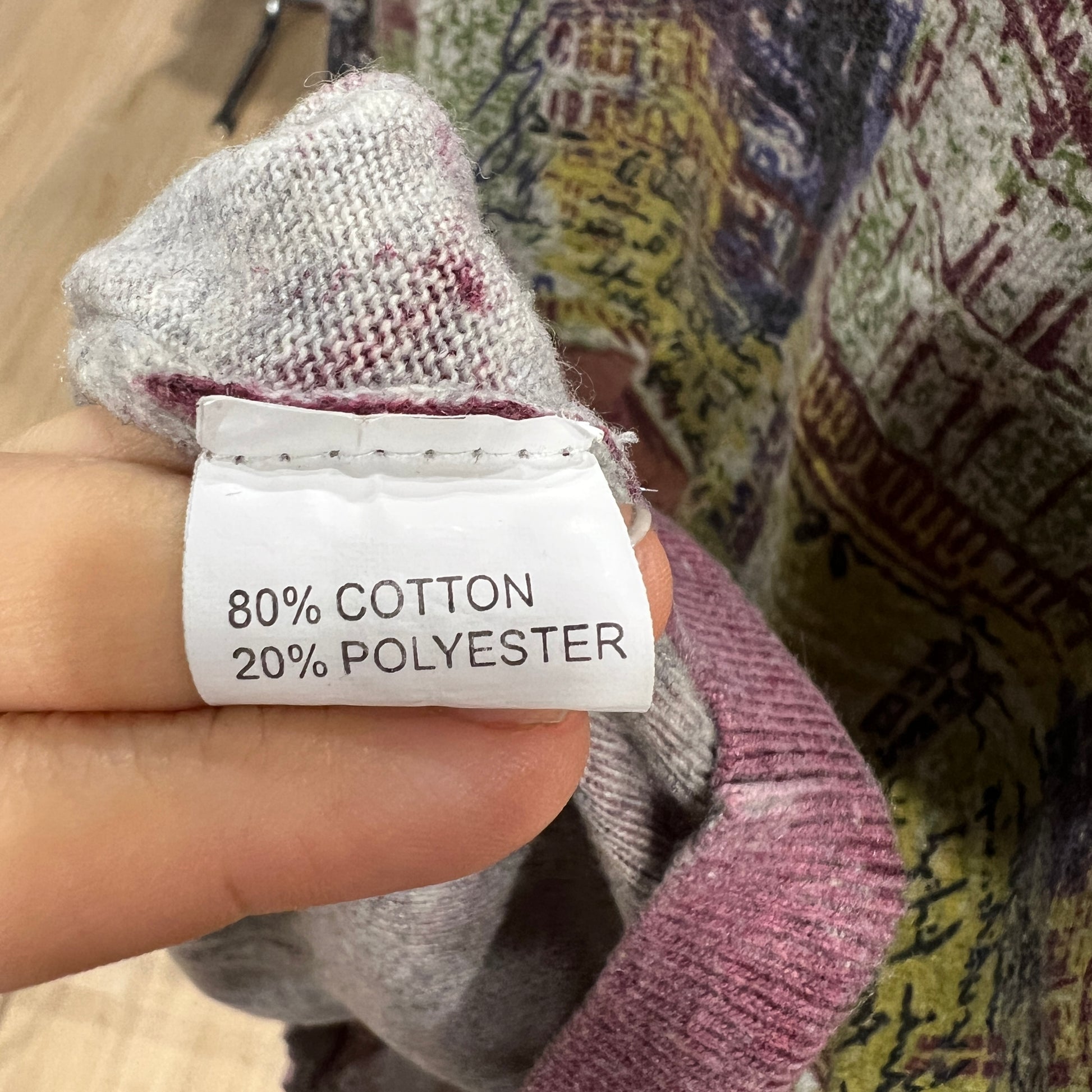 Hand holding a label with '80% Cotton, 20% Polyester' text against a textured fabric background