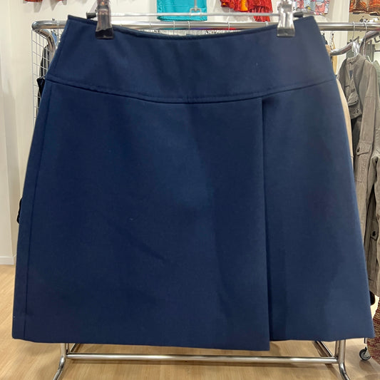 Front view of a navy blue A-line skirt with a clean structured design and a single front pleat, displayed on a hanger inside a vintage clothing store
