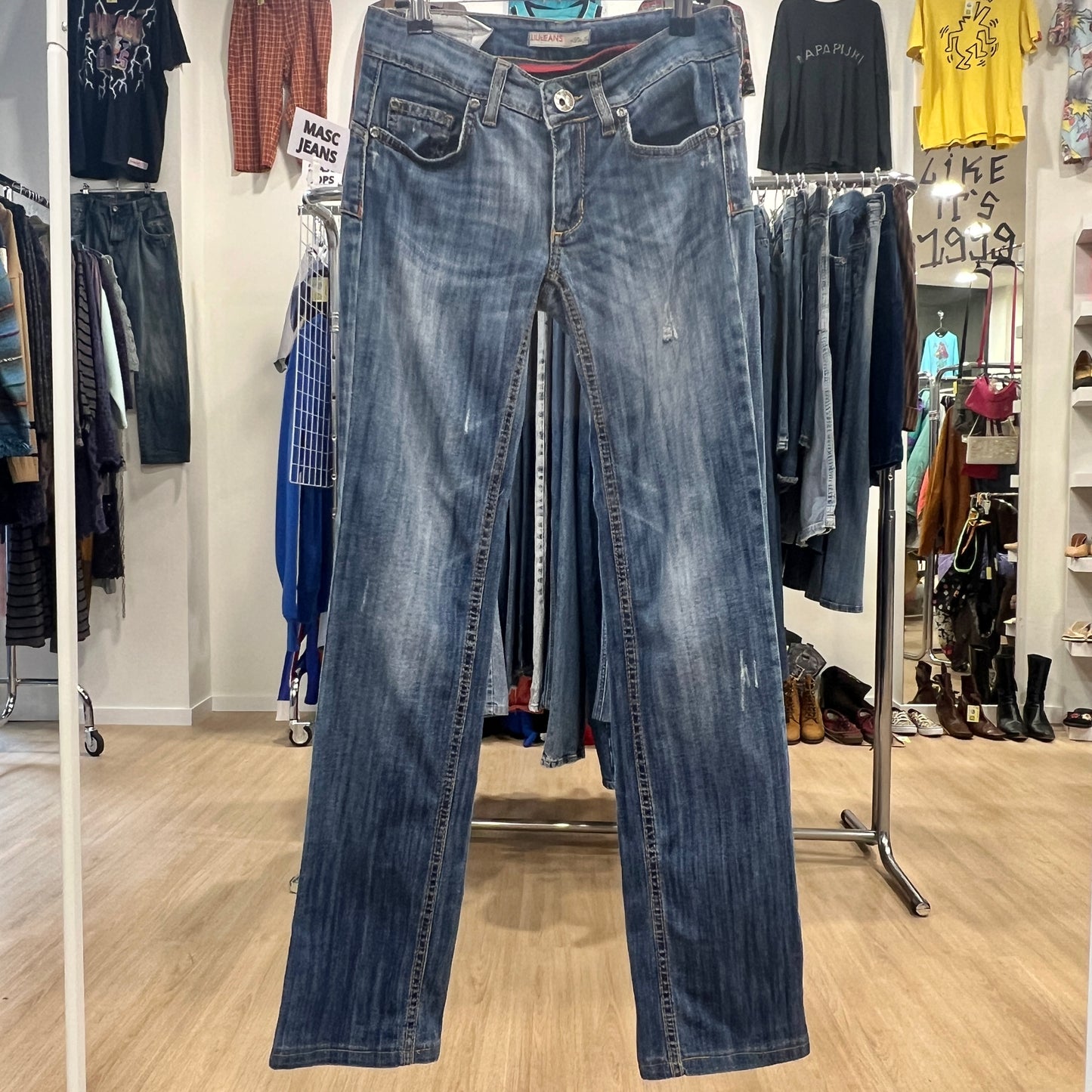 Blue jeans displayed on a rack in a store setting with various clothing items in the background