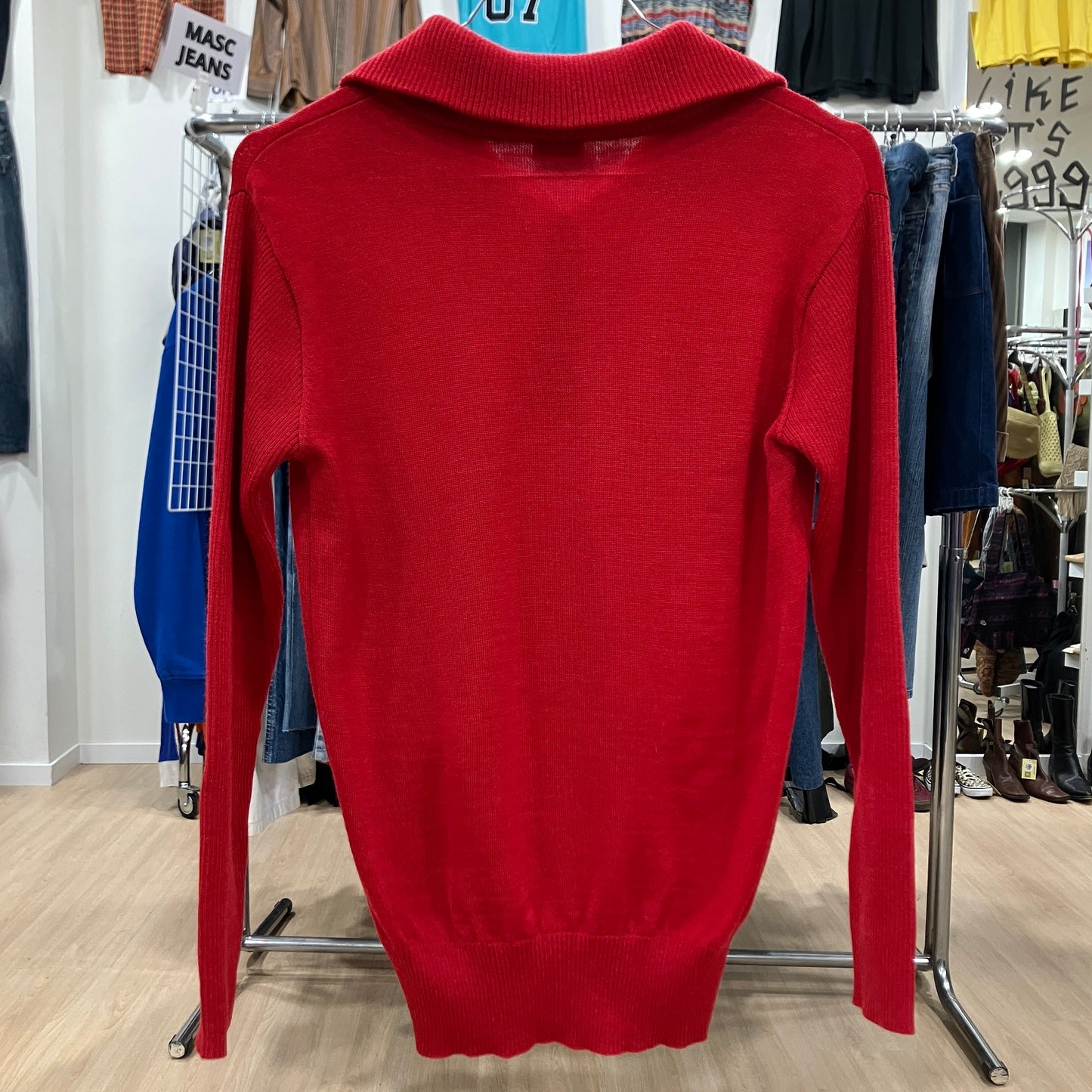Red sweater on a hanger in a store setting with various clothing items in the background