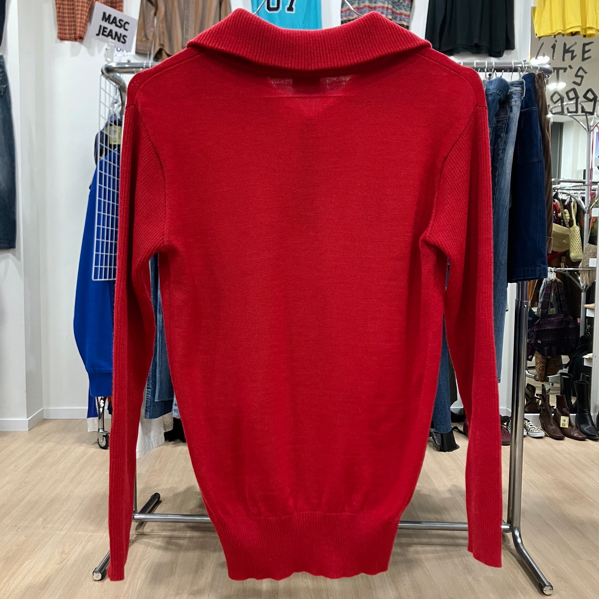 Red sweater on a hanger in a store setting with various clothing items in the background