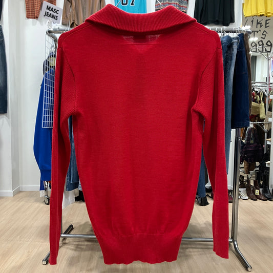 Red sweater on a hanger in a store setting with various clothing items in the background