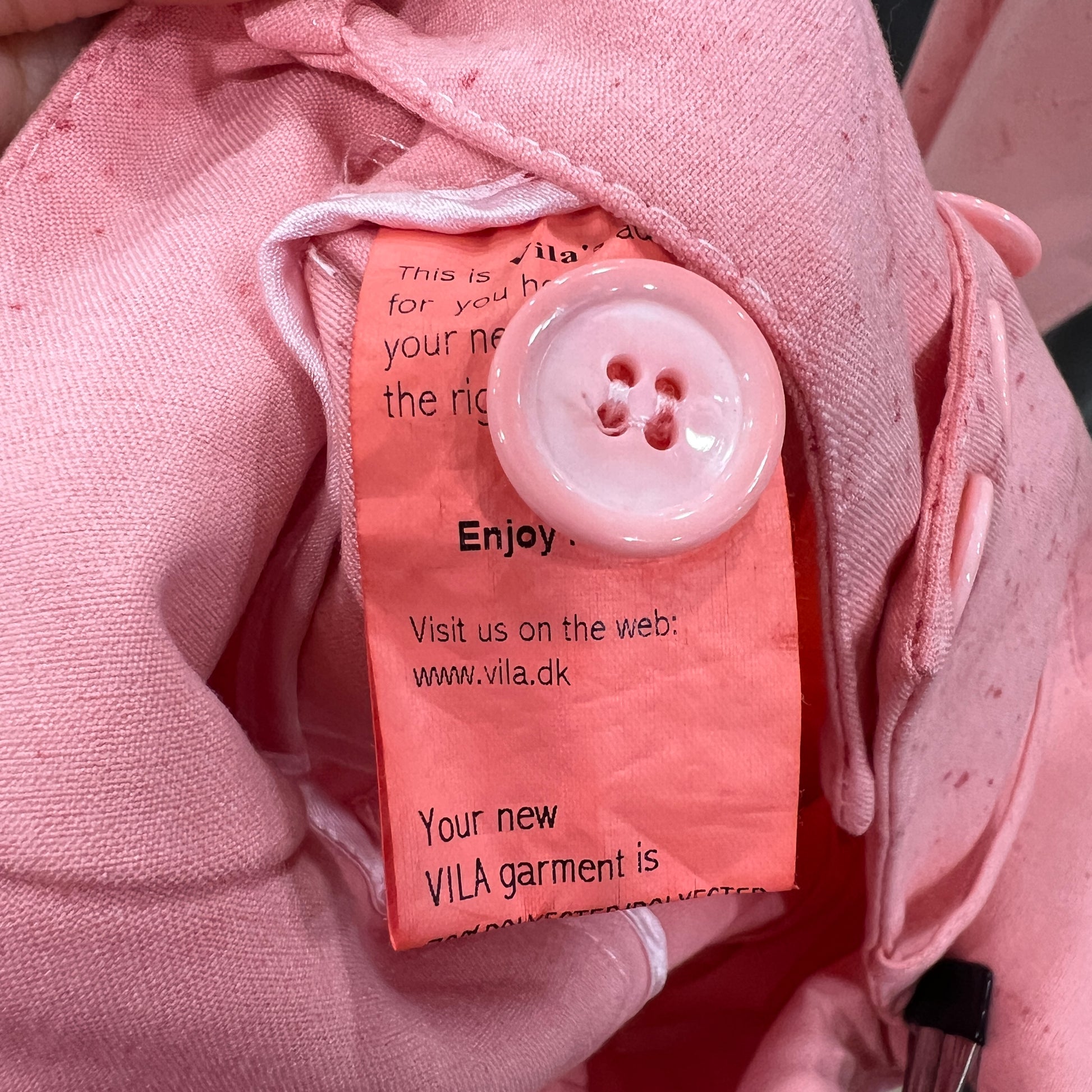 Pink garment with a button and VILA label on a pink background
