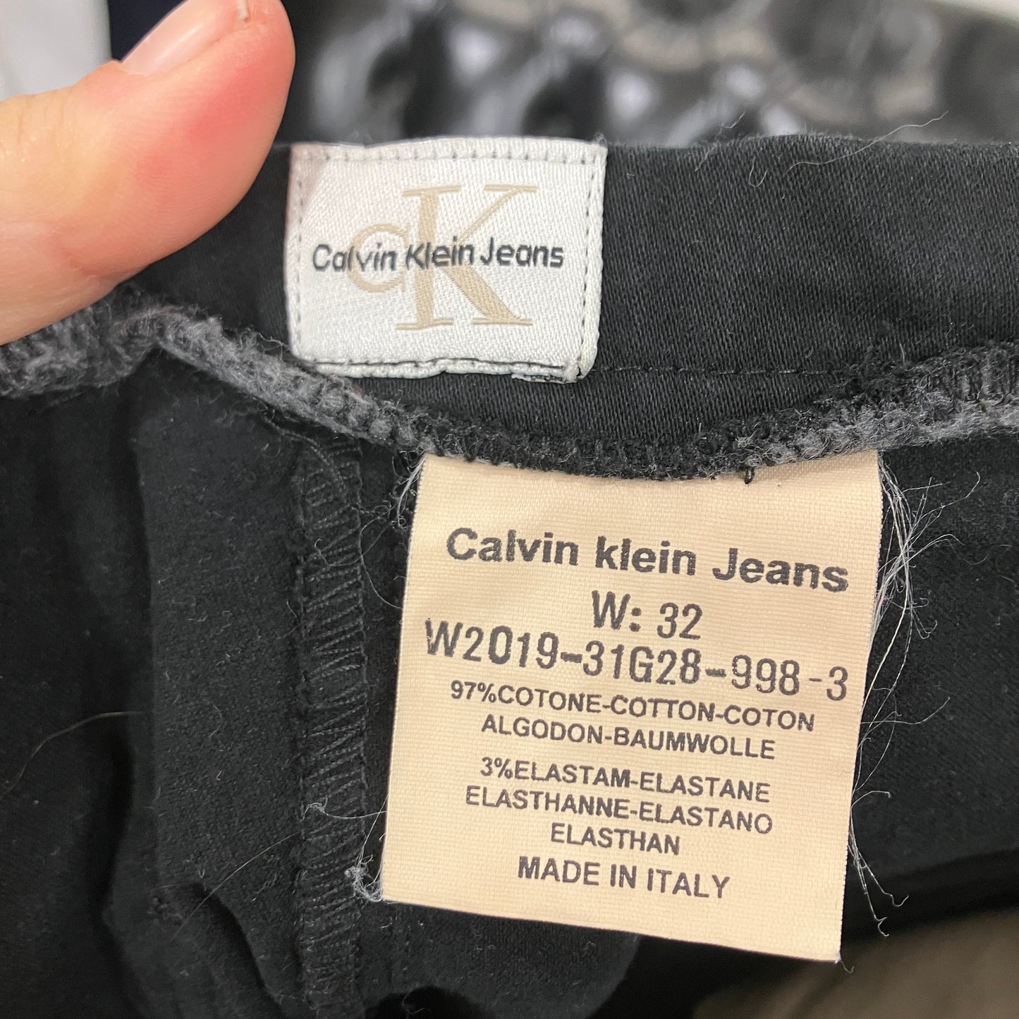 Calvin Klein Jeans label on a black garment with a hand holding it