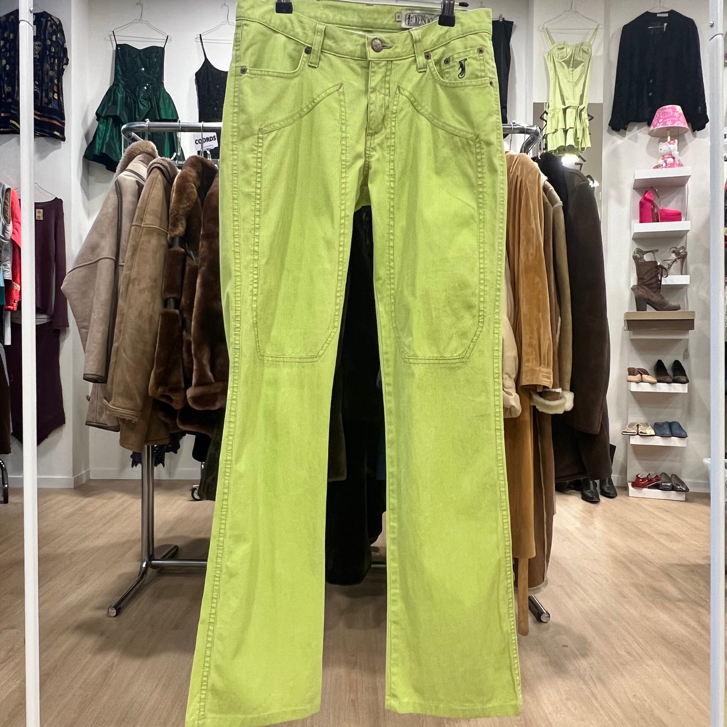 Bright green pants hanging in a clothing store with various garments in the background