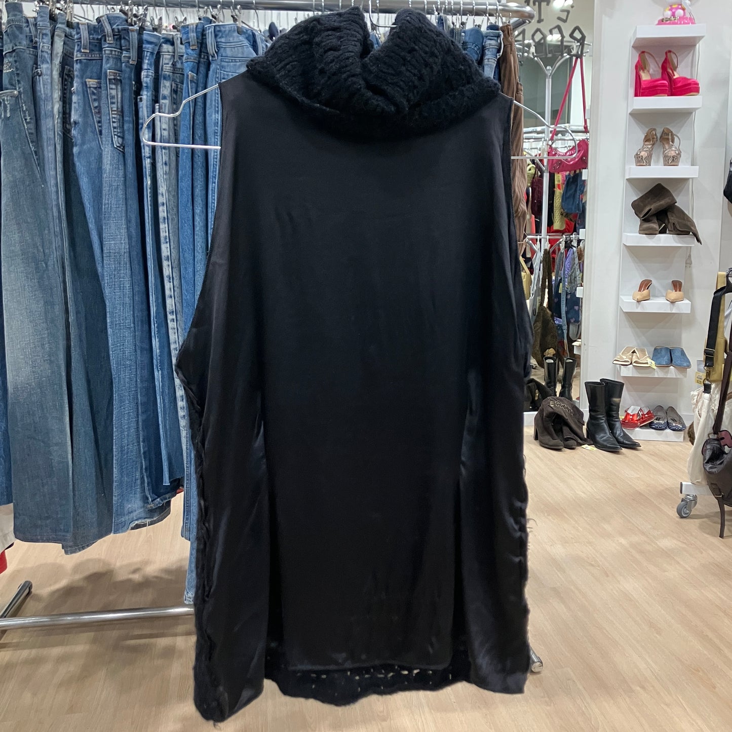 Black knitted vest on a hanger in a clothing store with racks of clothes in the background