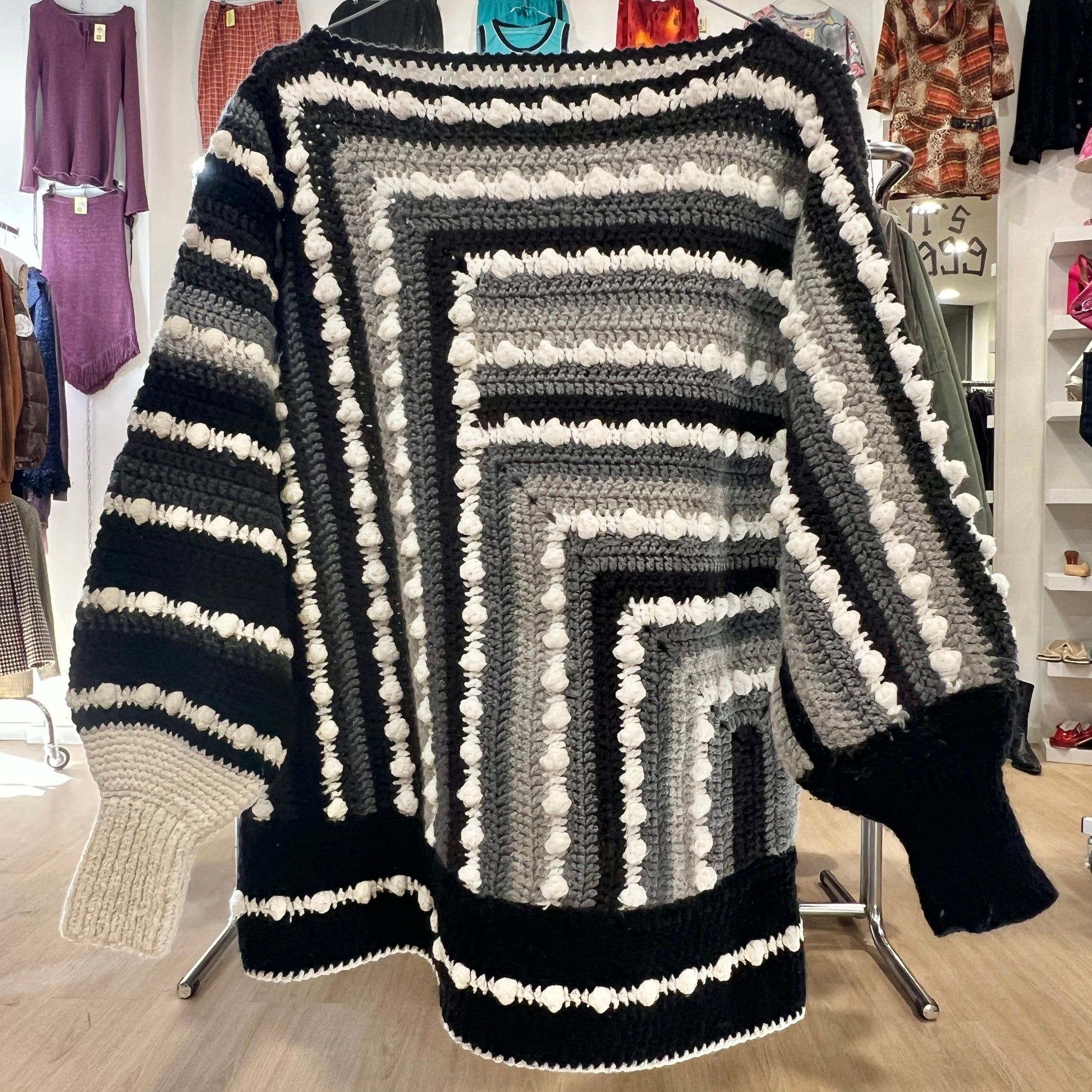 Black, gray, and white striped sweater with pom-poms on a rack in a store setting